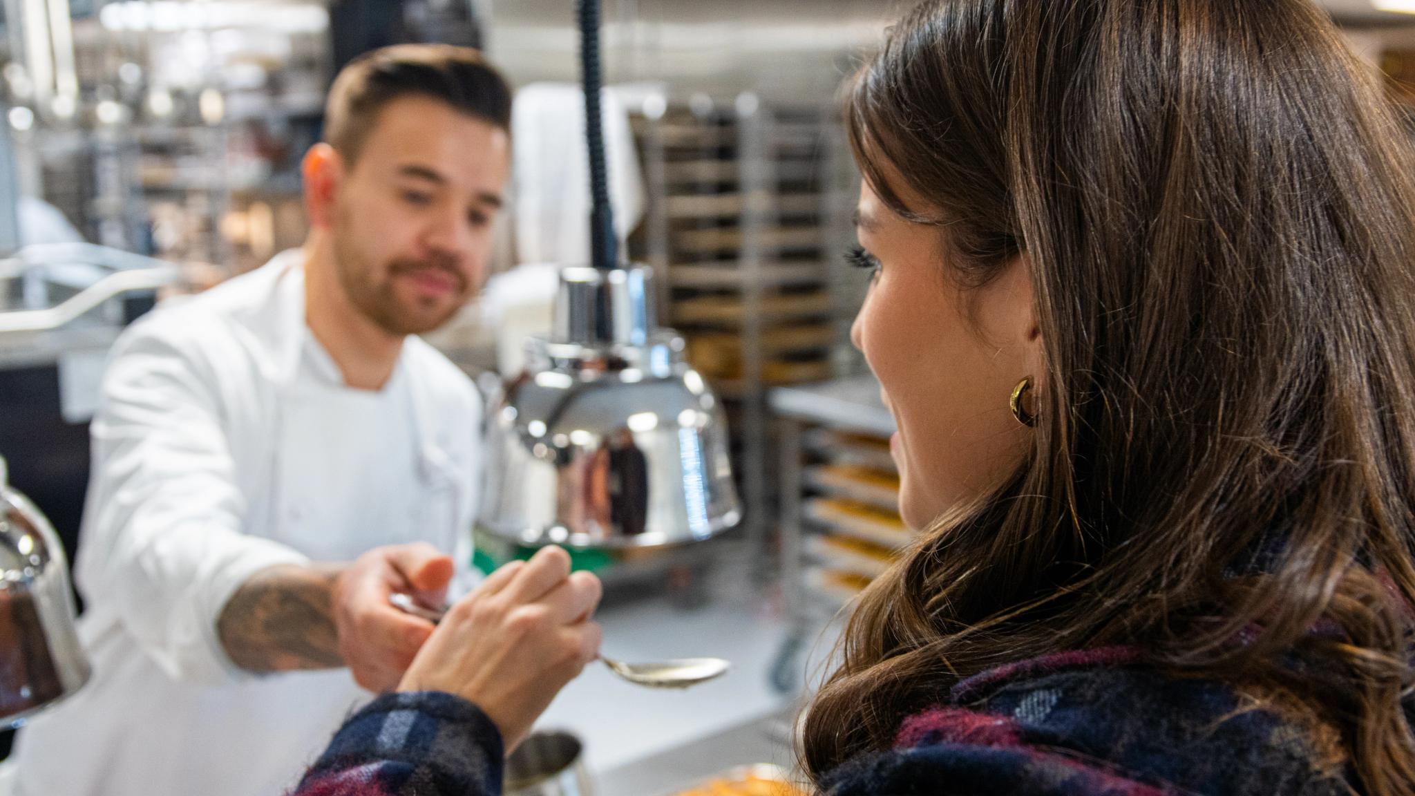 A women tastes food in an kitchen.