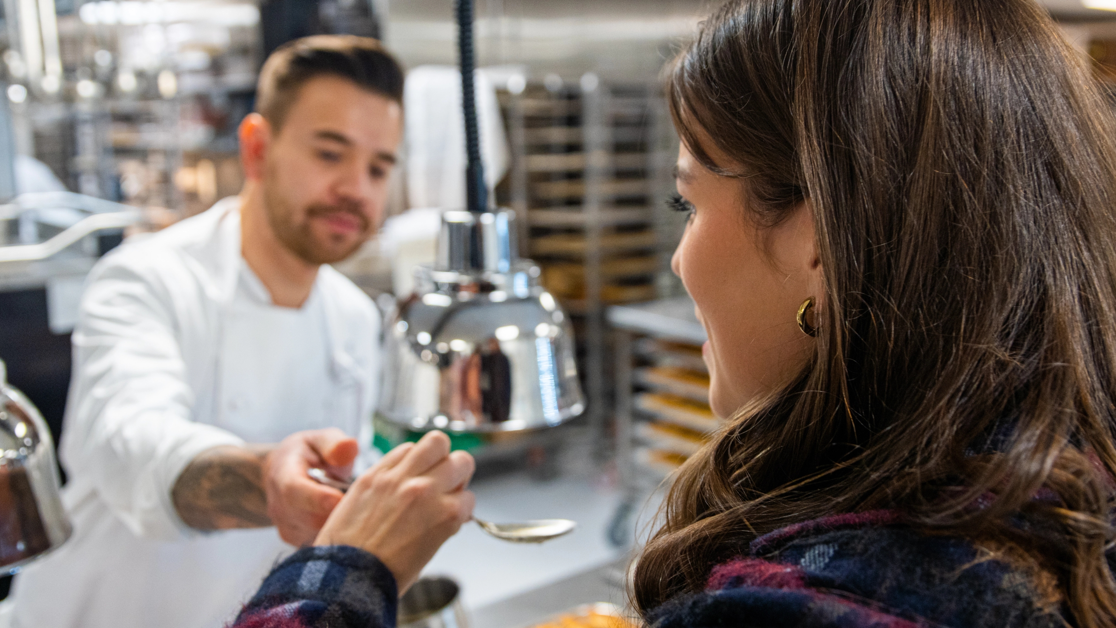 A women tastes food in an kitchen.