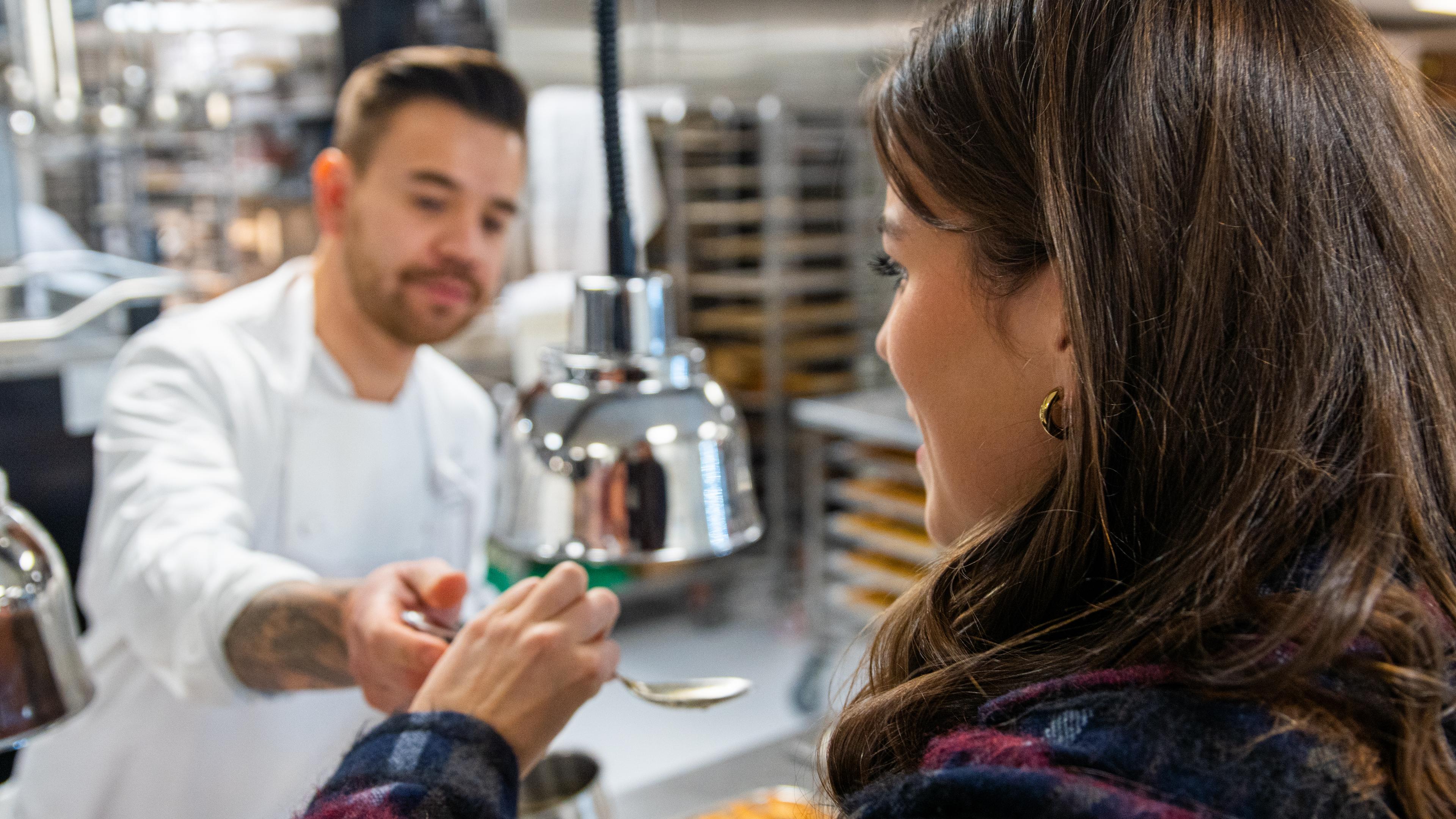 A women tastes food in an kitchen.