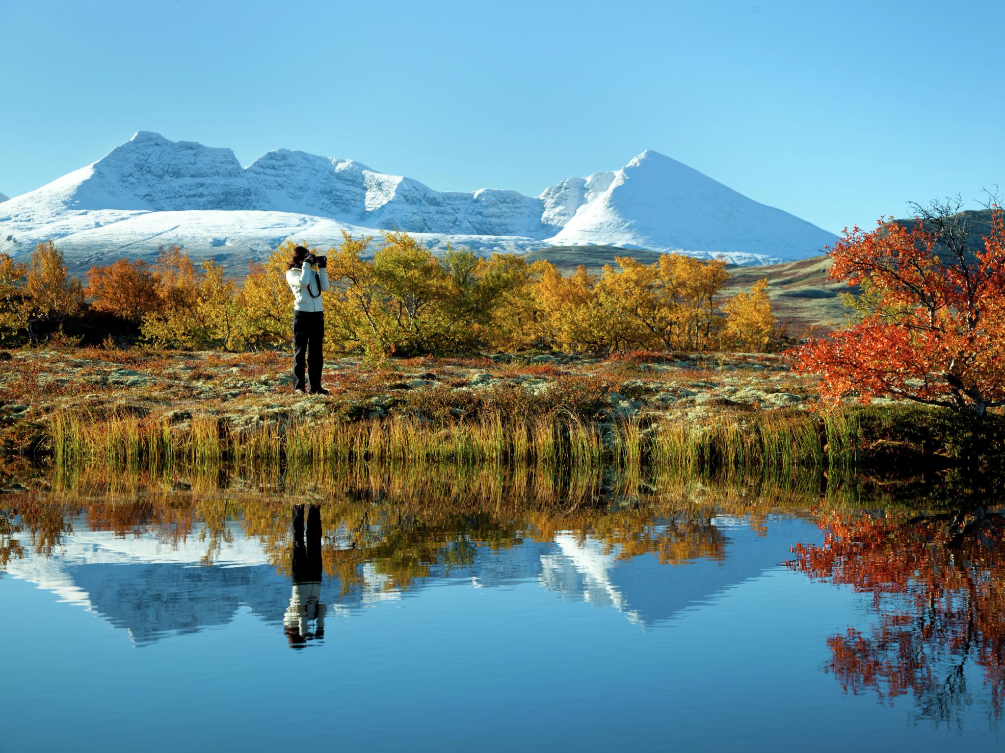 Photographie d’un lac et des feuillages automnaux dans le parc national des Rondane, en Norvège de l'Est. Montagnes enneigées à l’arrière-plan.