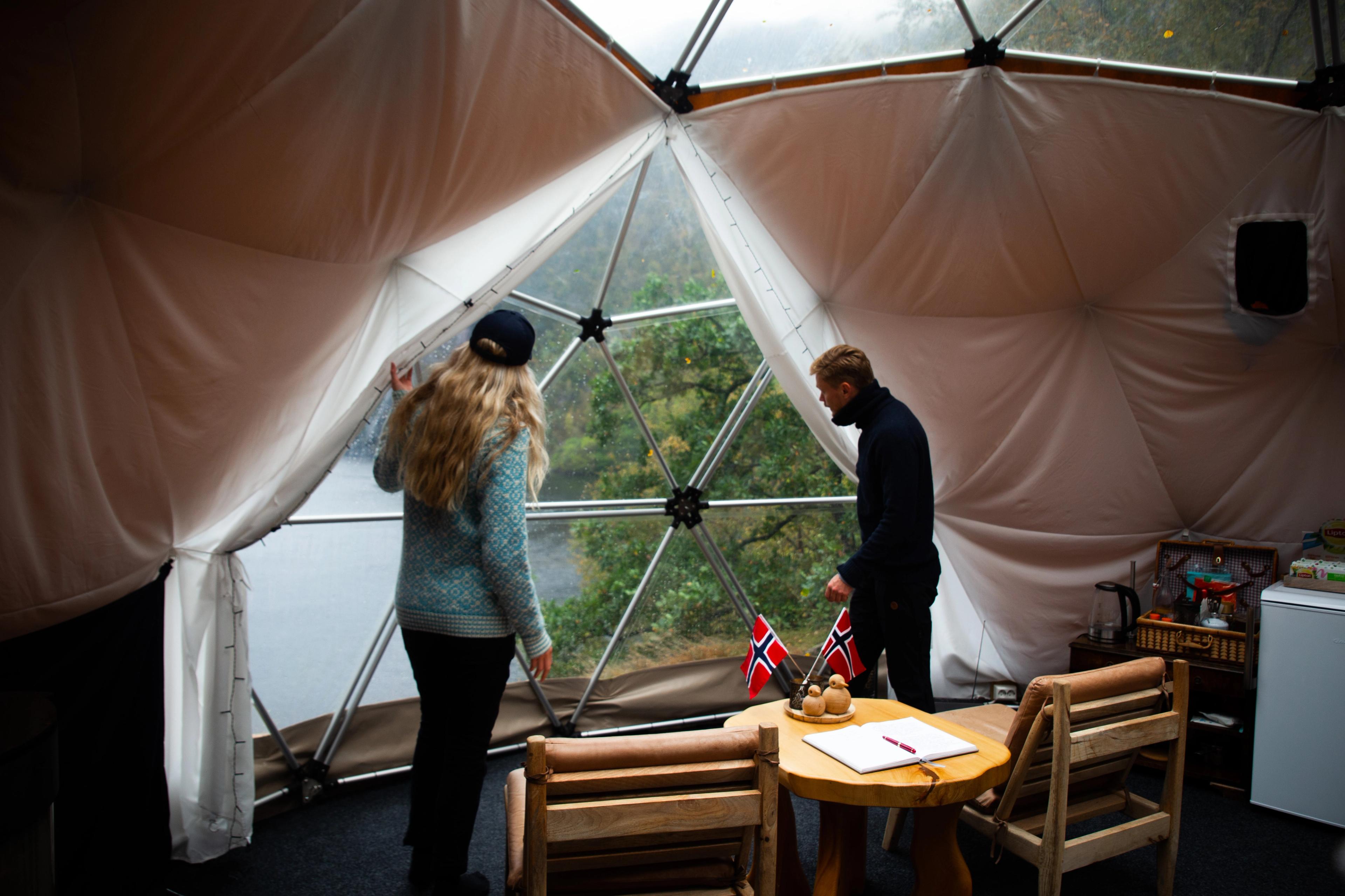 Two people in a dome, looking out at nature.