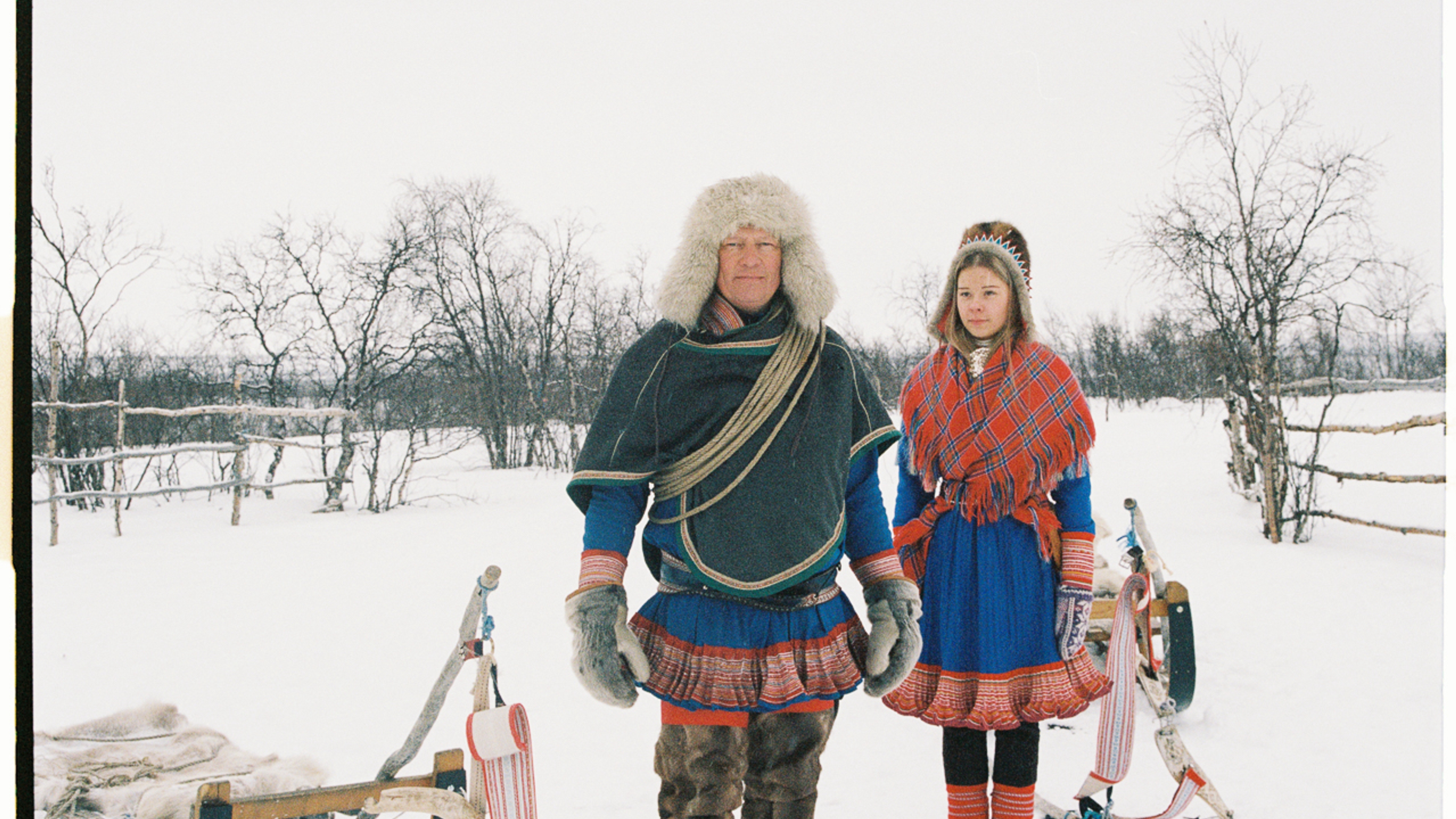 Two Sami people in a snow covered landscape.
