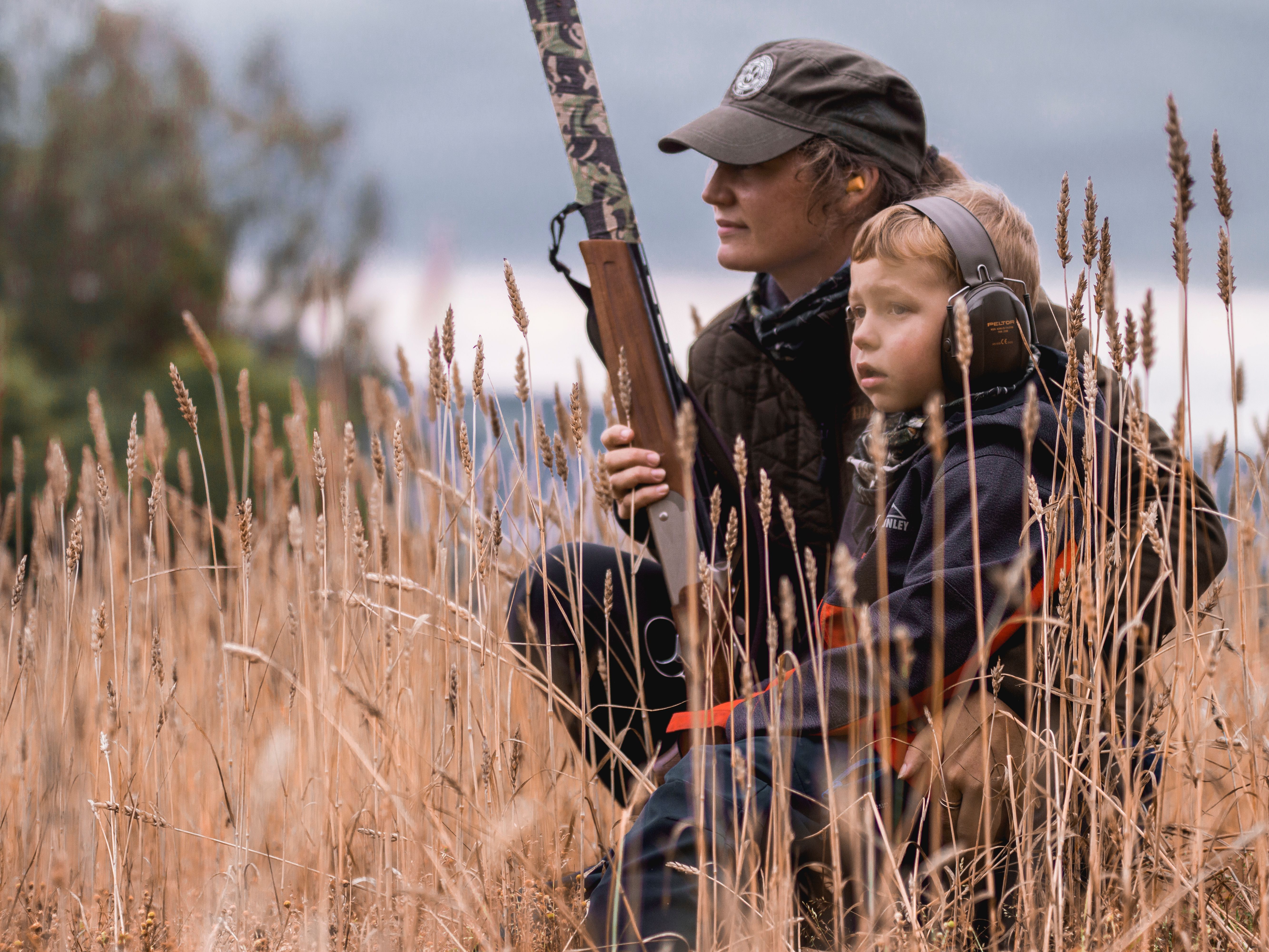 En mor og hennes sønn sitter i det lange gresset og venter mens de er på jakt i skogen om høsten