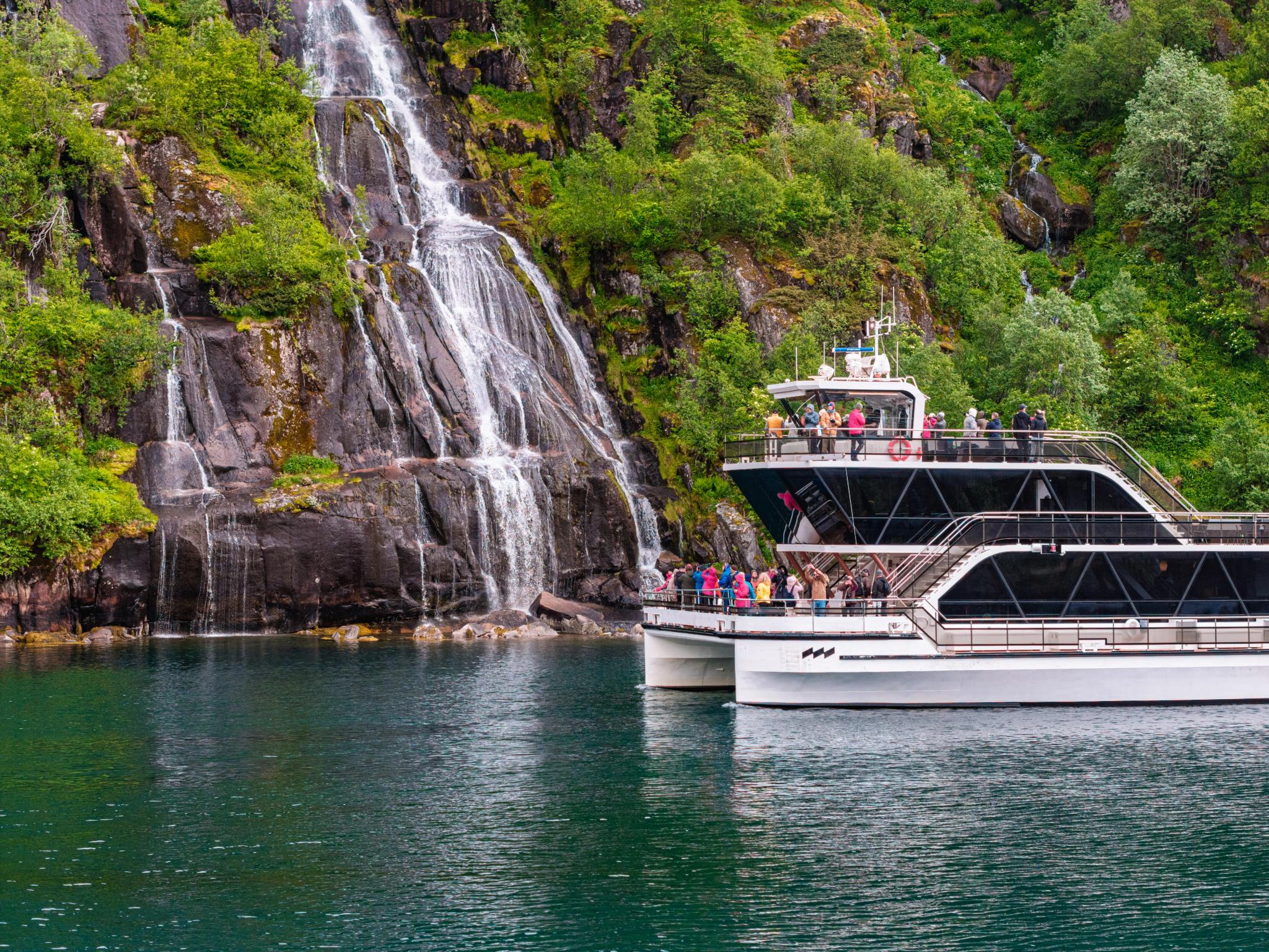 Cruise ship passengers viewing waterfall in Norwegian fjord