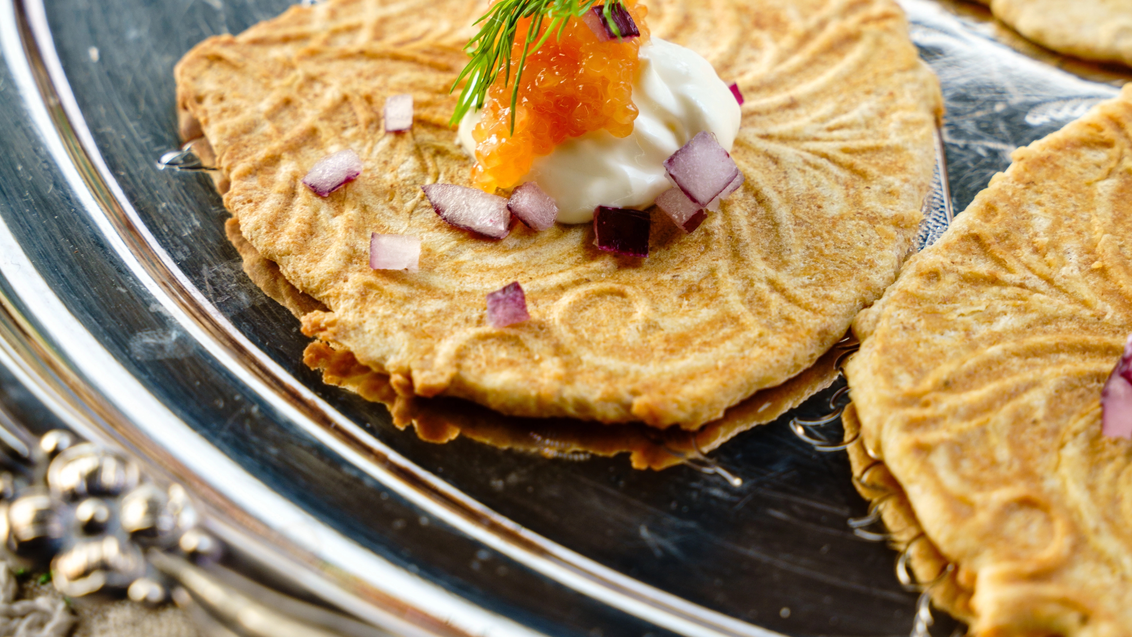 Krumkaker on a silver plate with salmon roe and sour cream.