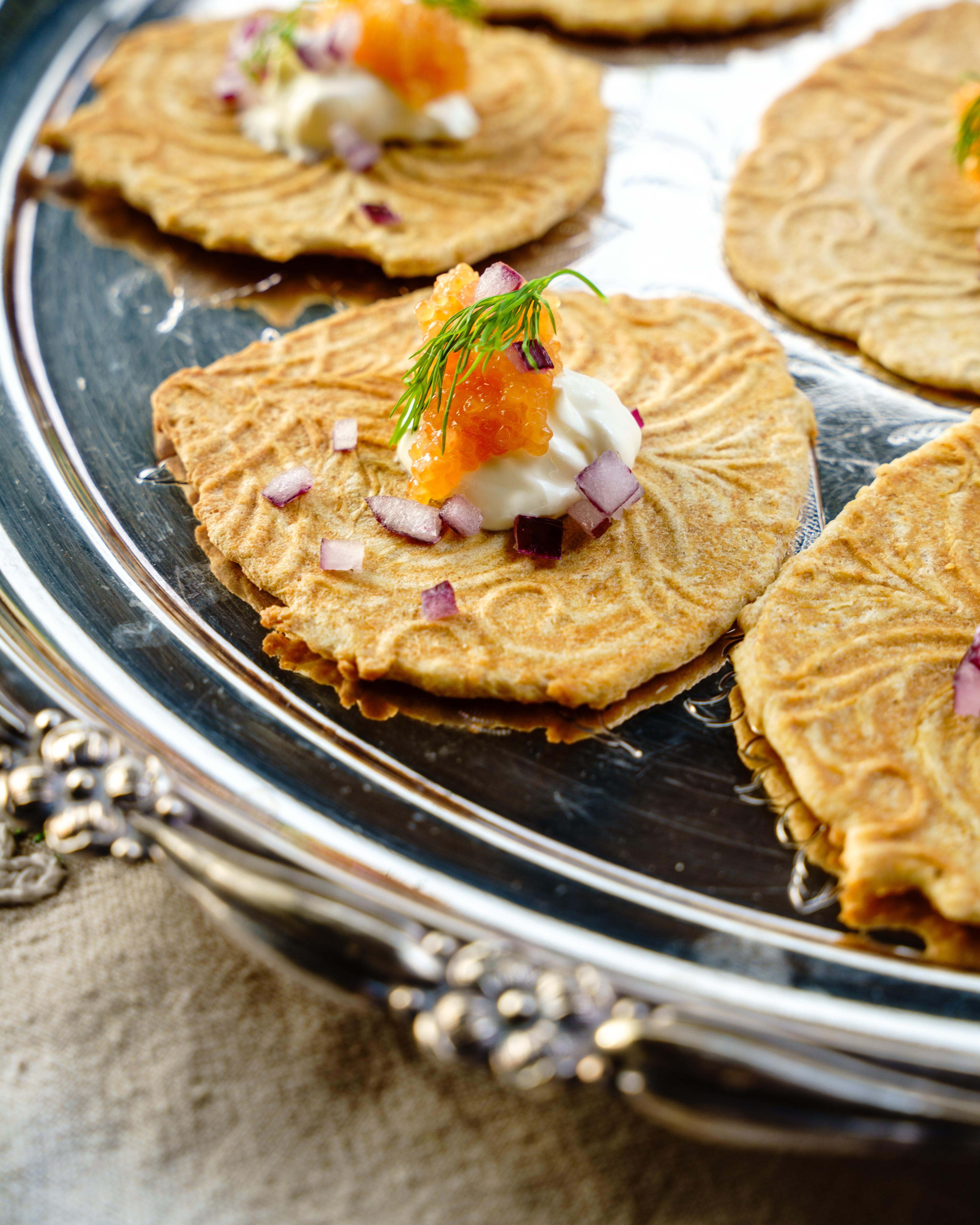 Krumkaker on a silver plate with salmon roe and sour cream.