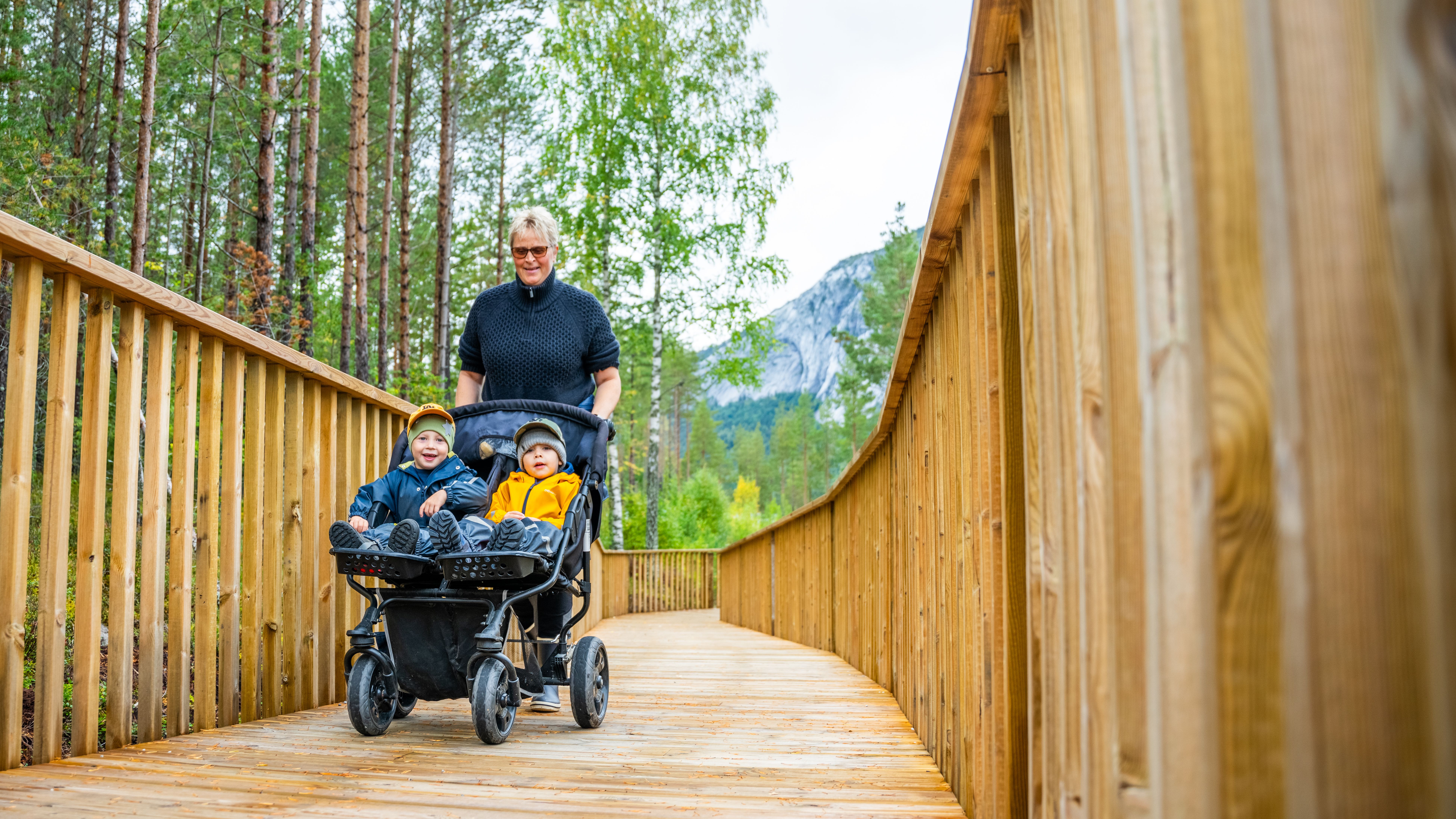 Person with two kids in a pram walking the treetop road in Fyresdal