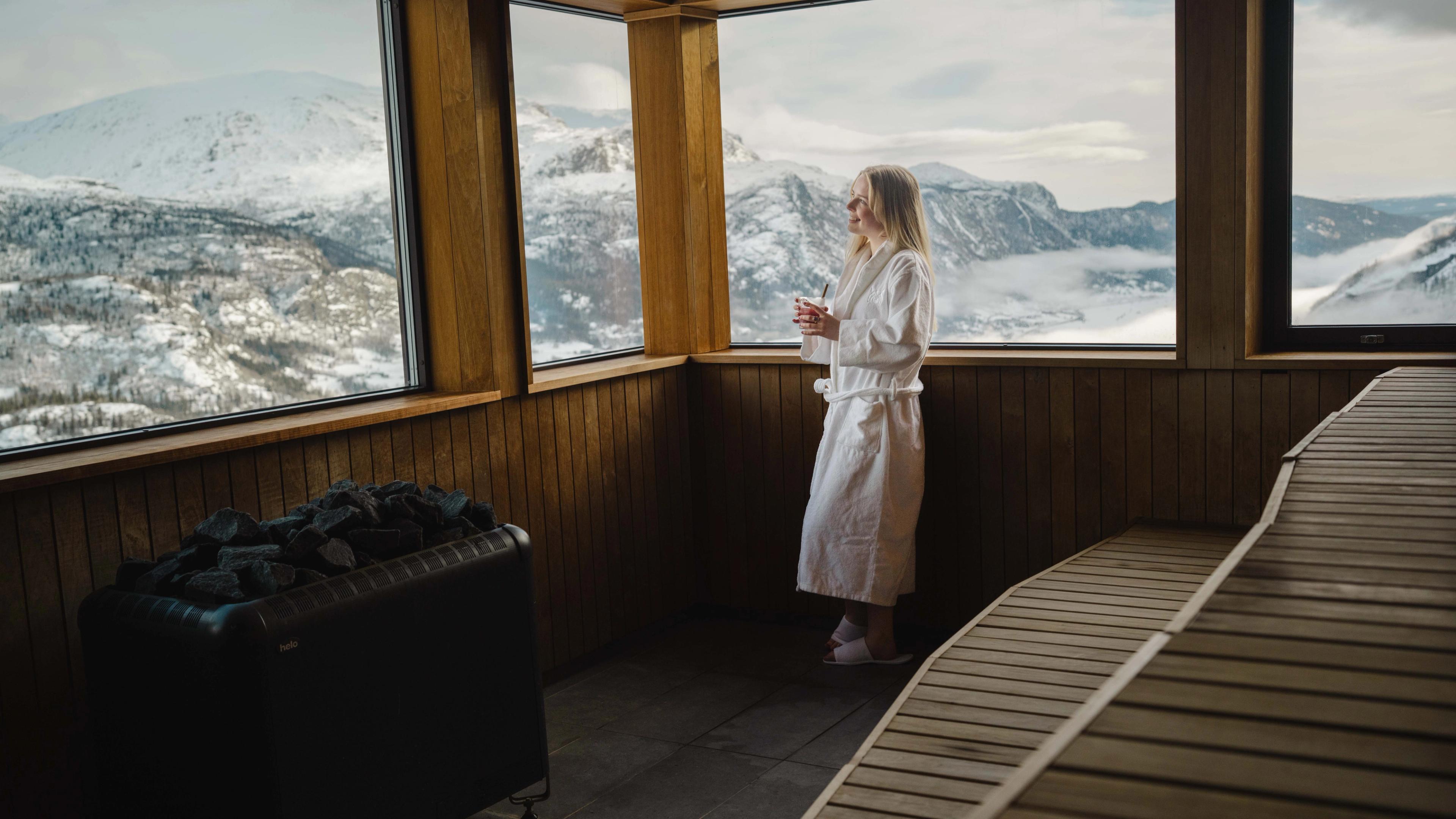 A girl relaxes inside the spa at Skarsnuten, while a skier glides down the slopes in the background