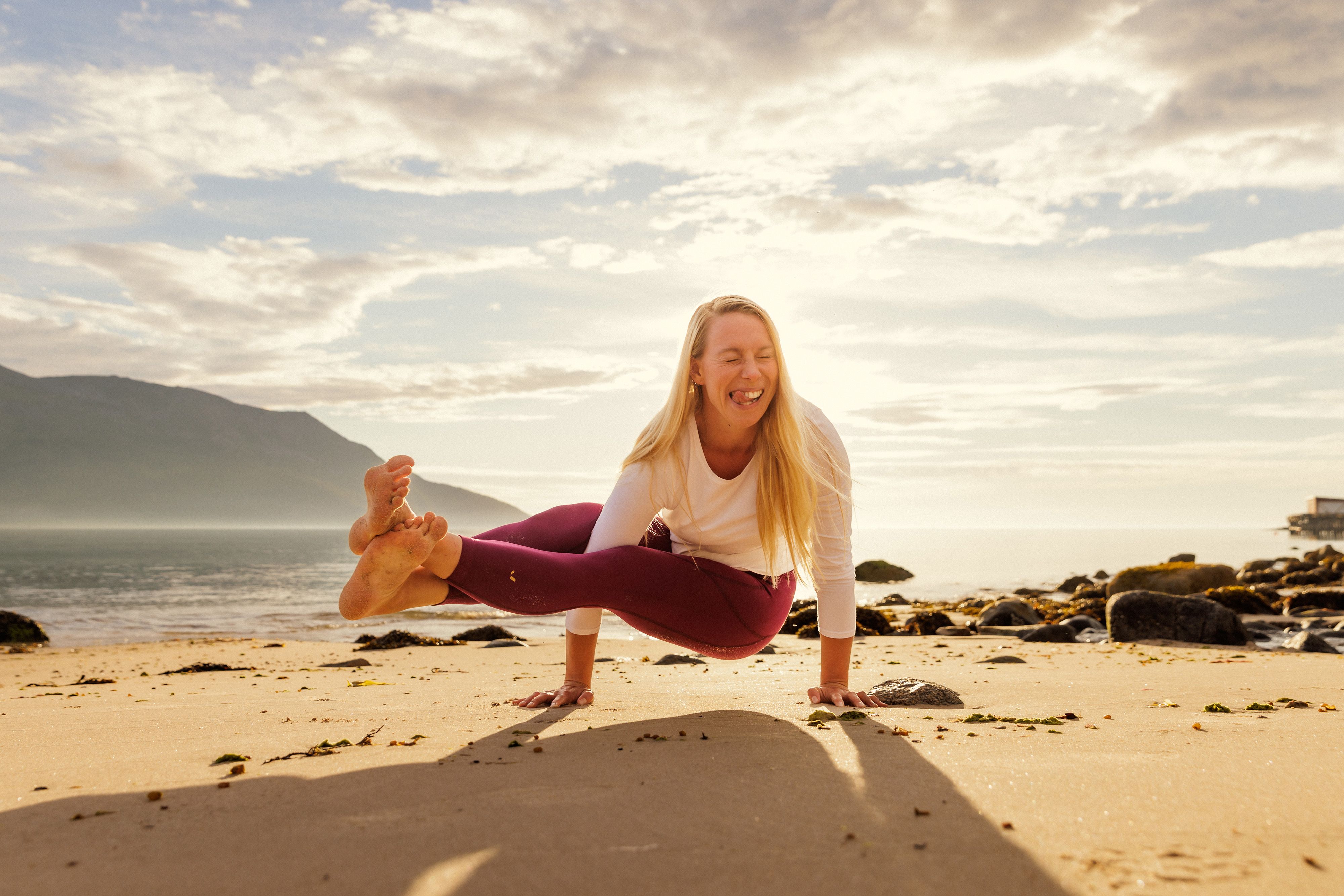 A woman smiling as she is doing yoga on the beach in the midnight sun, Northern Norway.