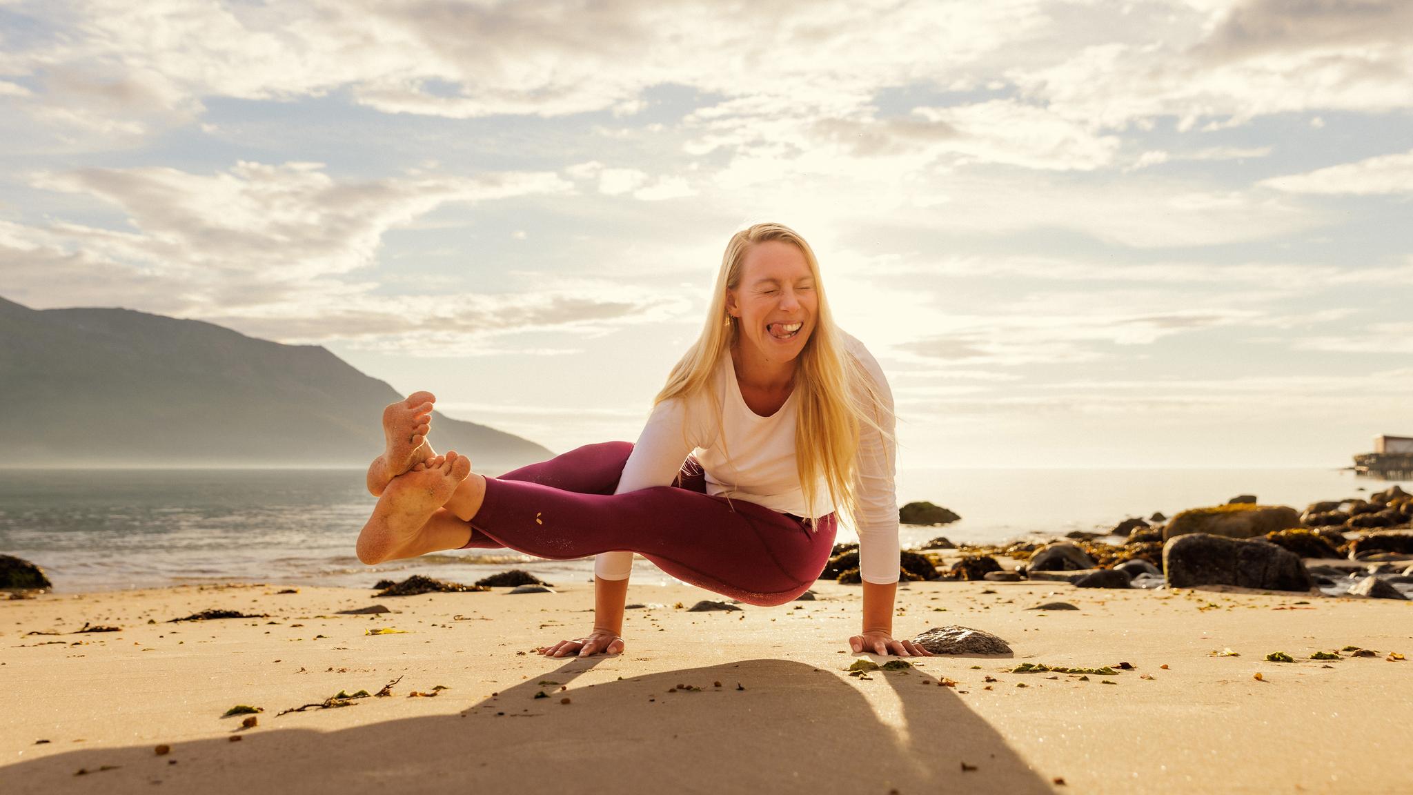 A woman smiling as she is doing yoga on the beach in the midnight sun, Northern Norway.