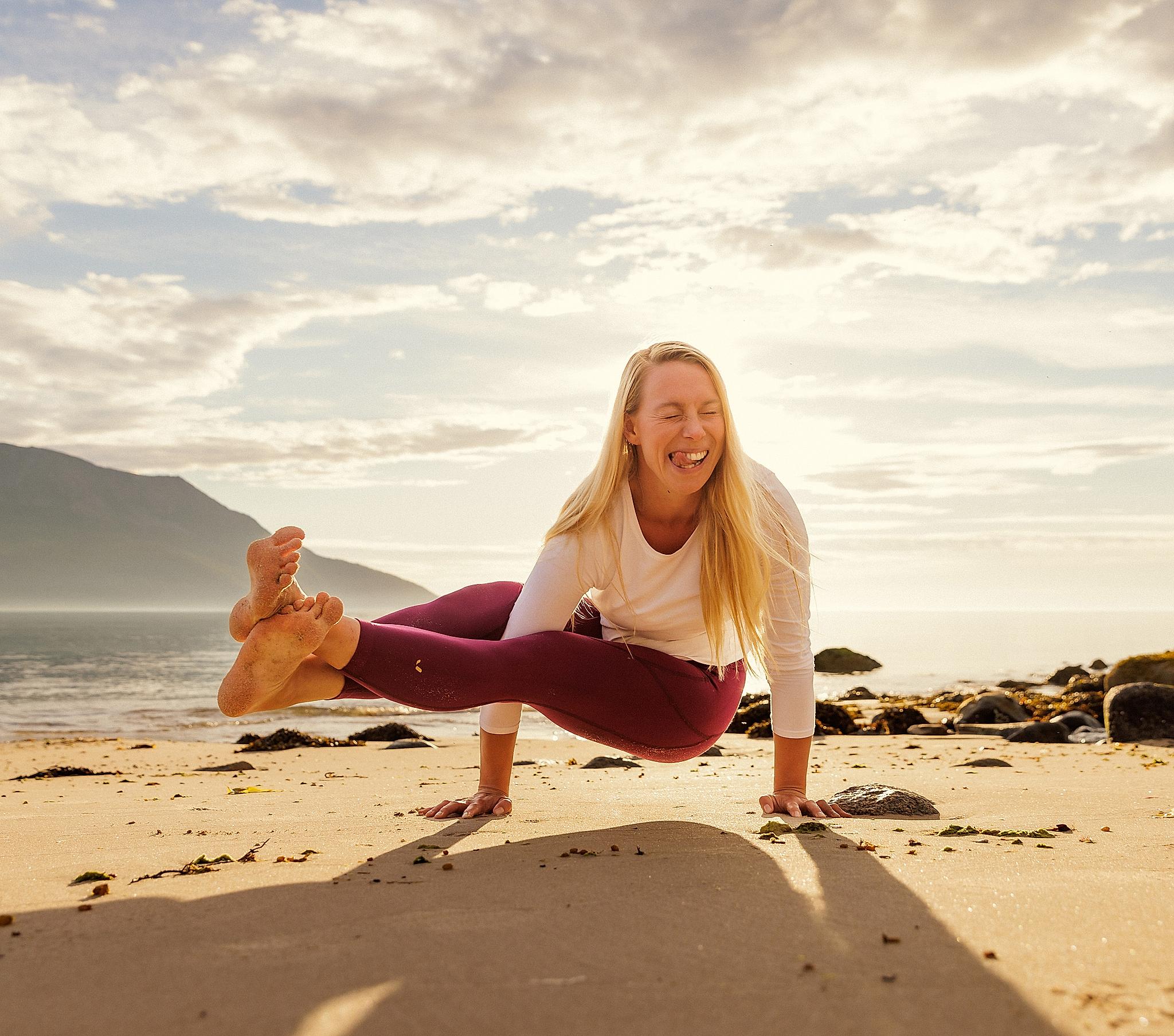 Ei dame smiler å gjør yoga på stranden i midnattsolen i Nord-Norge