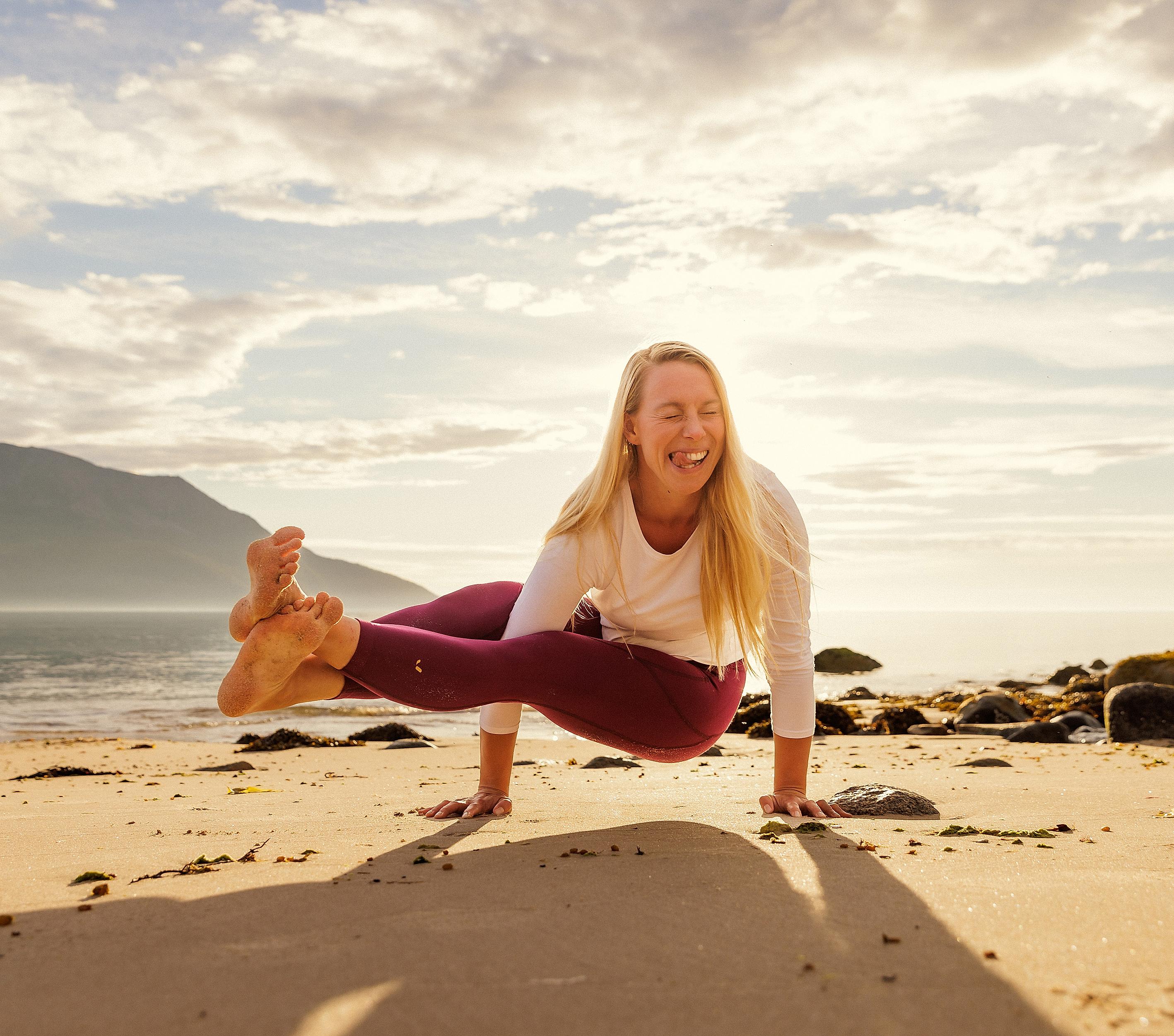 A woman smiling as she is doing yoga on the beach in the midnight sun, Northern Norway.