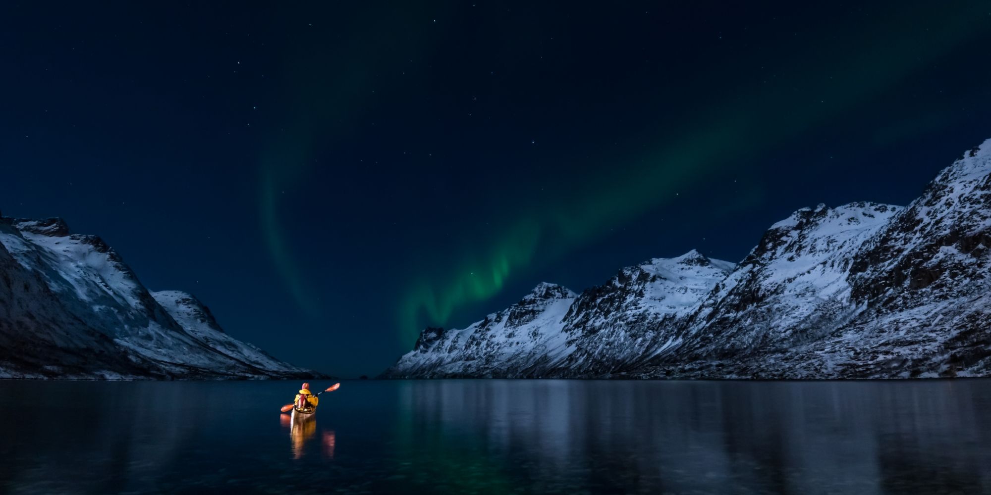 A woman paddling under the northern lights in Lofoten