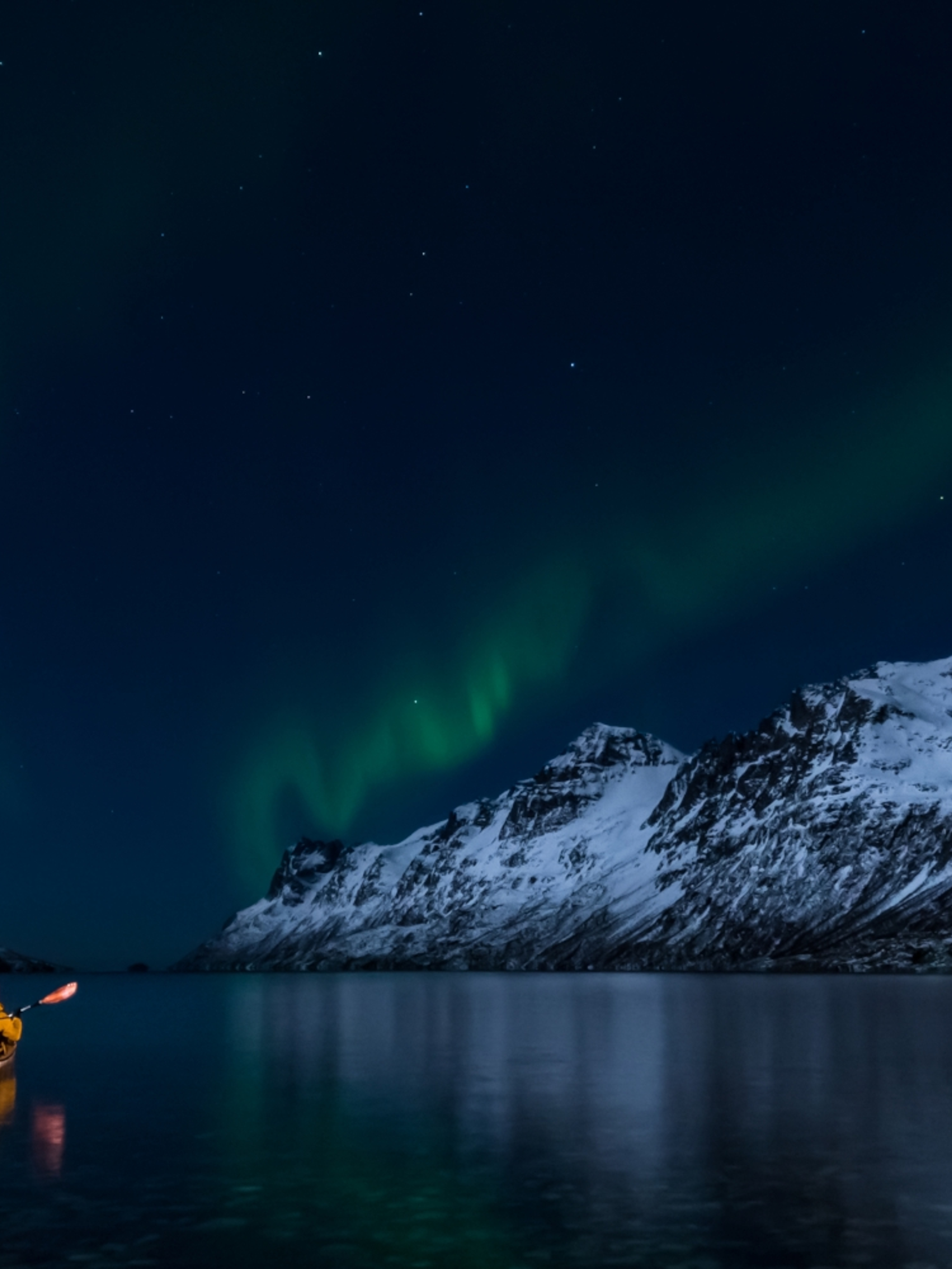 A woman paddling under the northern lights in Lofoten
