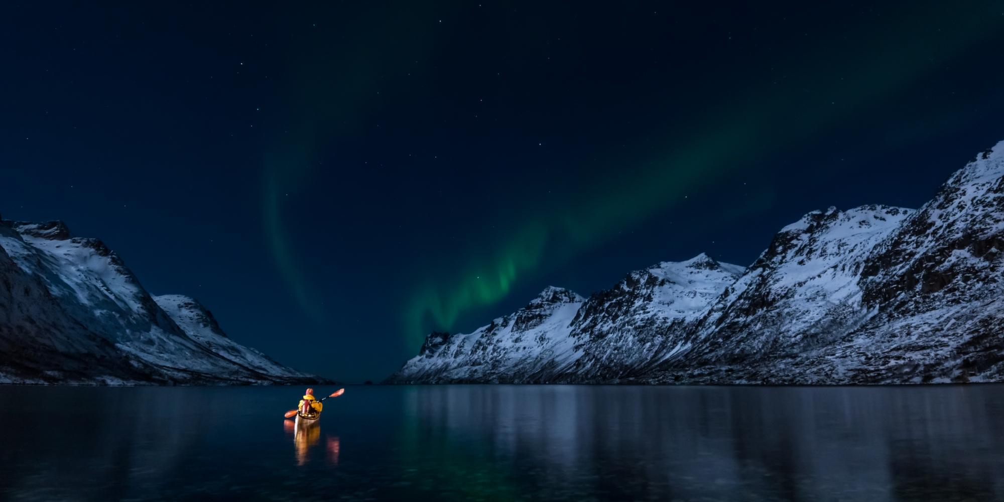 A woman paddling under the northern lights in Lofoten