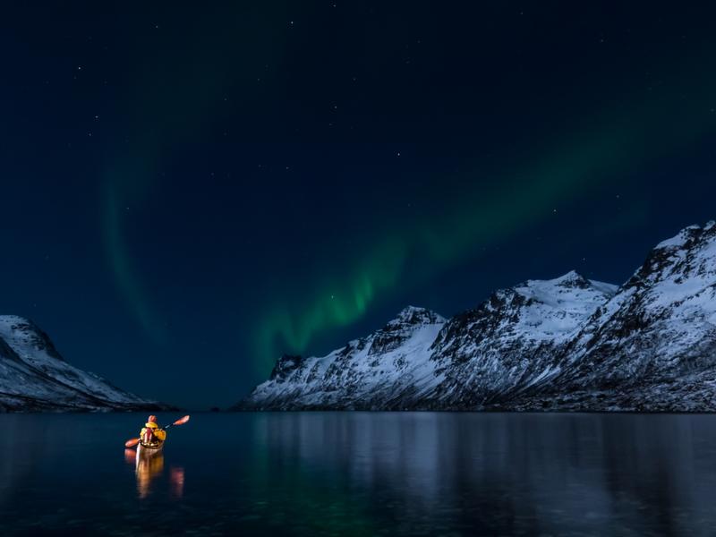 A woman paddling under the northern lights in Lofoten