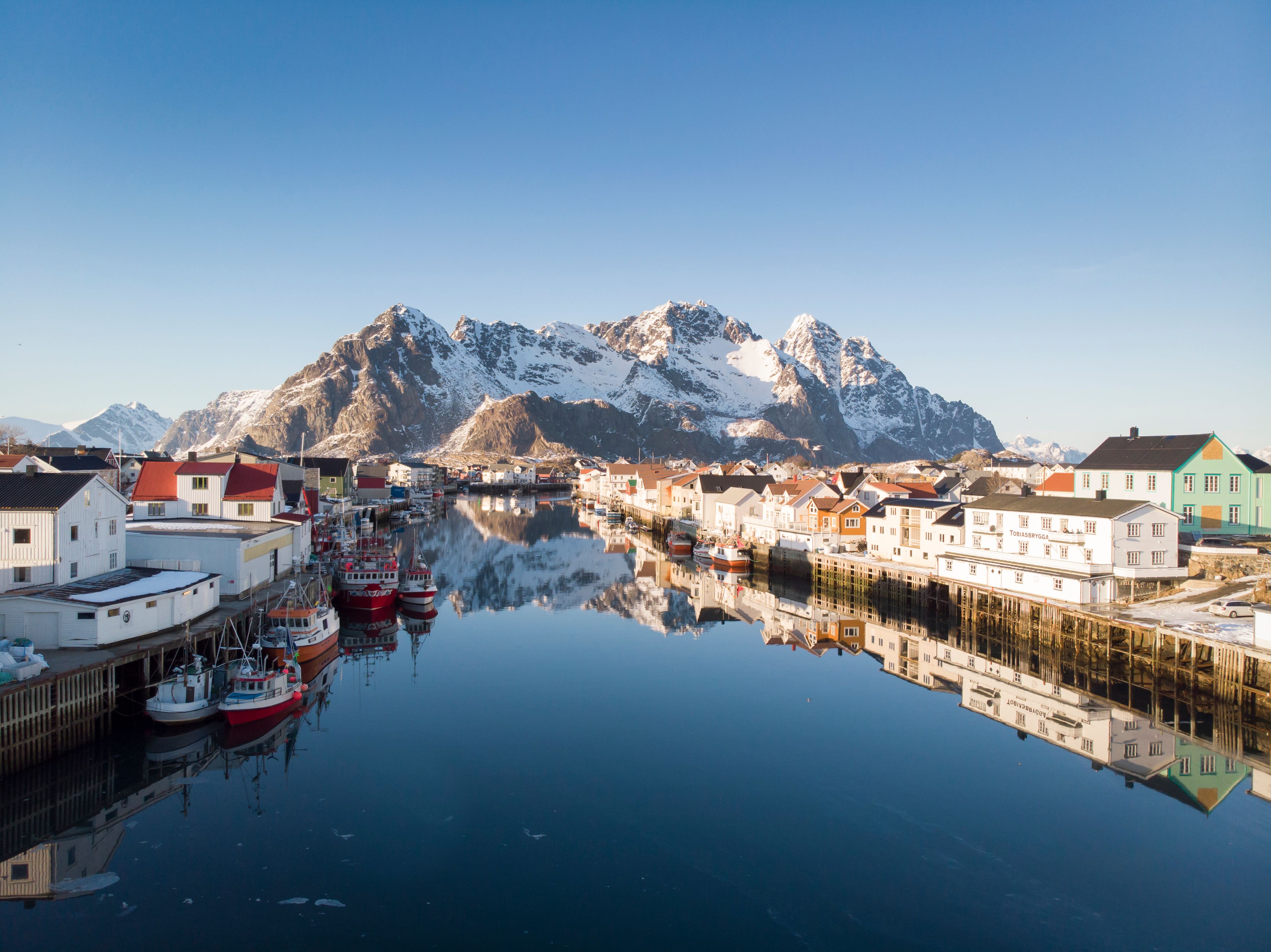 Houten huizen, vissersboten en besneeuwde bergen in Henningsvær op de Lofoten in Noord-Noorwegen op een zonnige winterdag