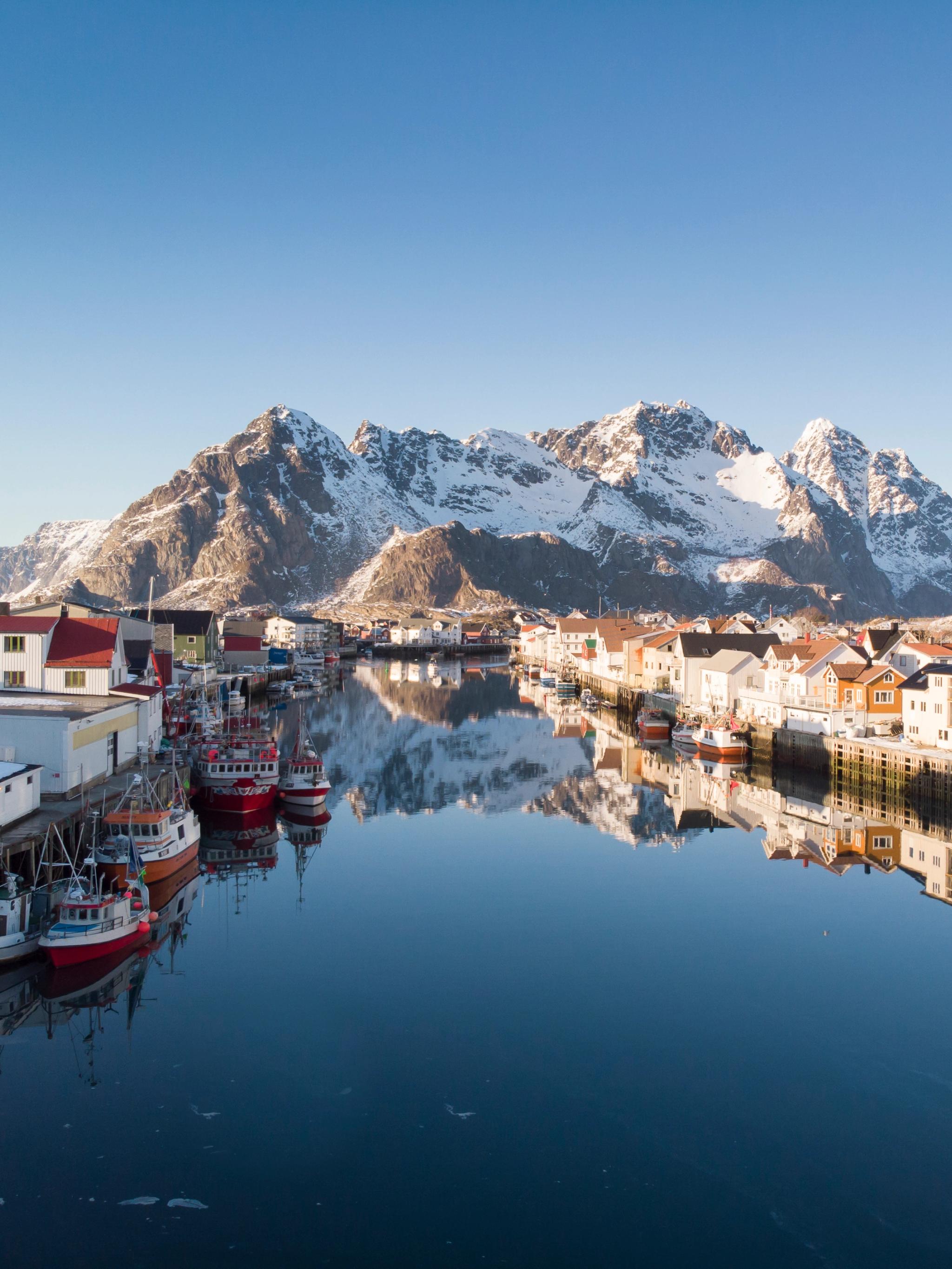 Wooden houses, fishing boats and snowcapped mountains, Henningsvær in certified Sustainable Destination Lofoten, Northern Norway