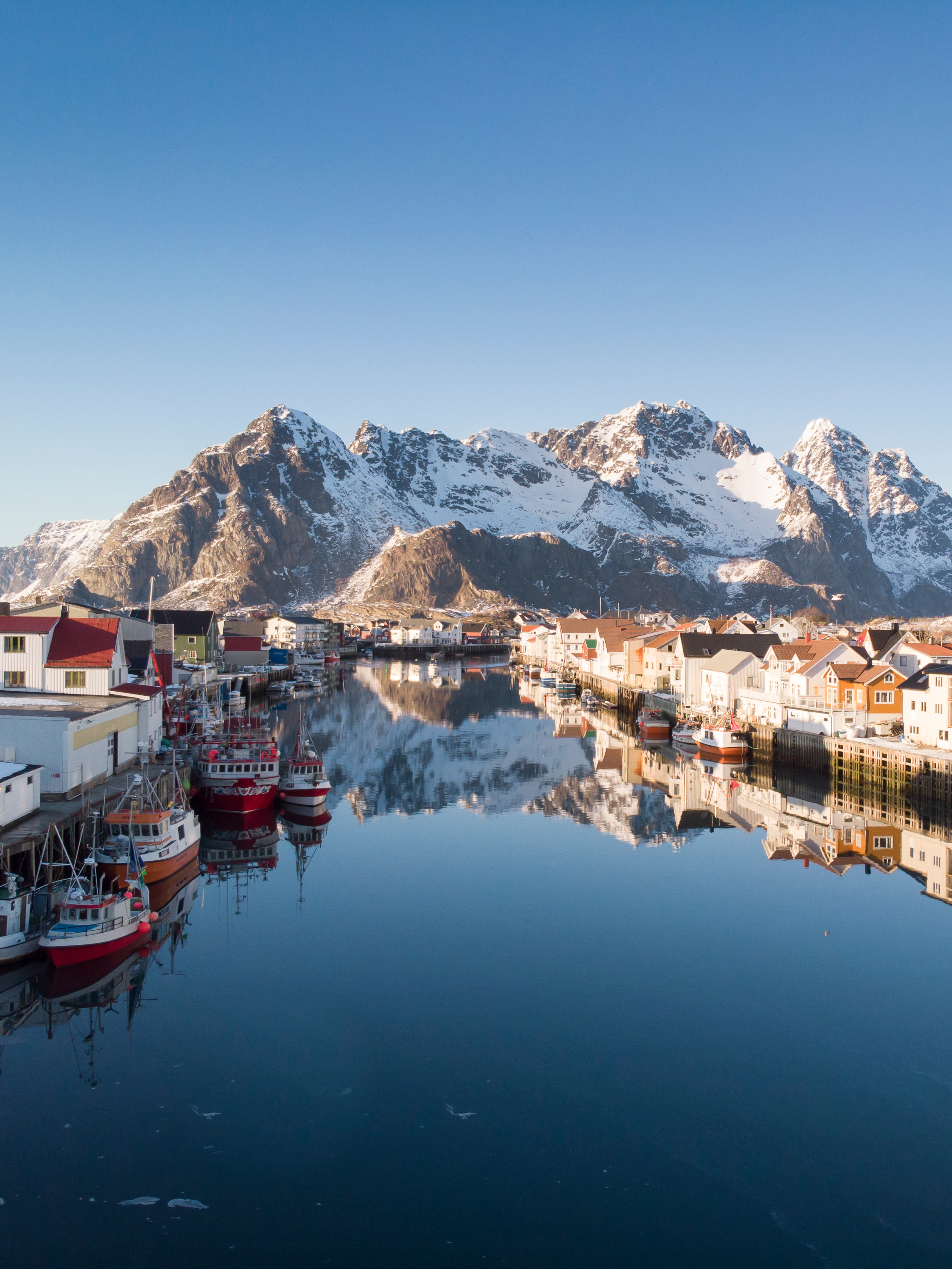 Wooden houses, fishing boats and snowcapped mountains, Henningsvær in certified Sustainable Destination Lofoten, Northern Norway