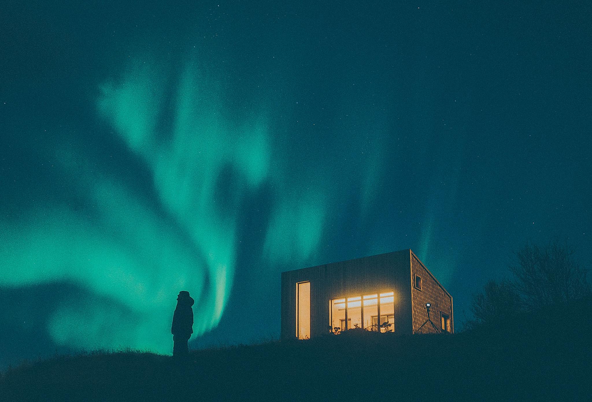 En person ser på nordlyset ved en bygning i Bodø i Nord-Norge