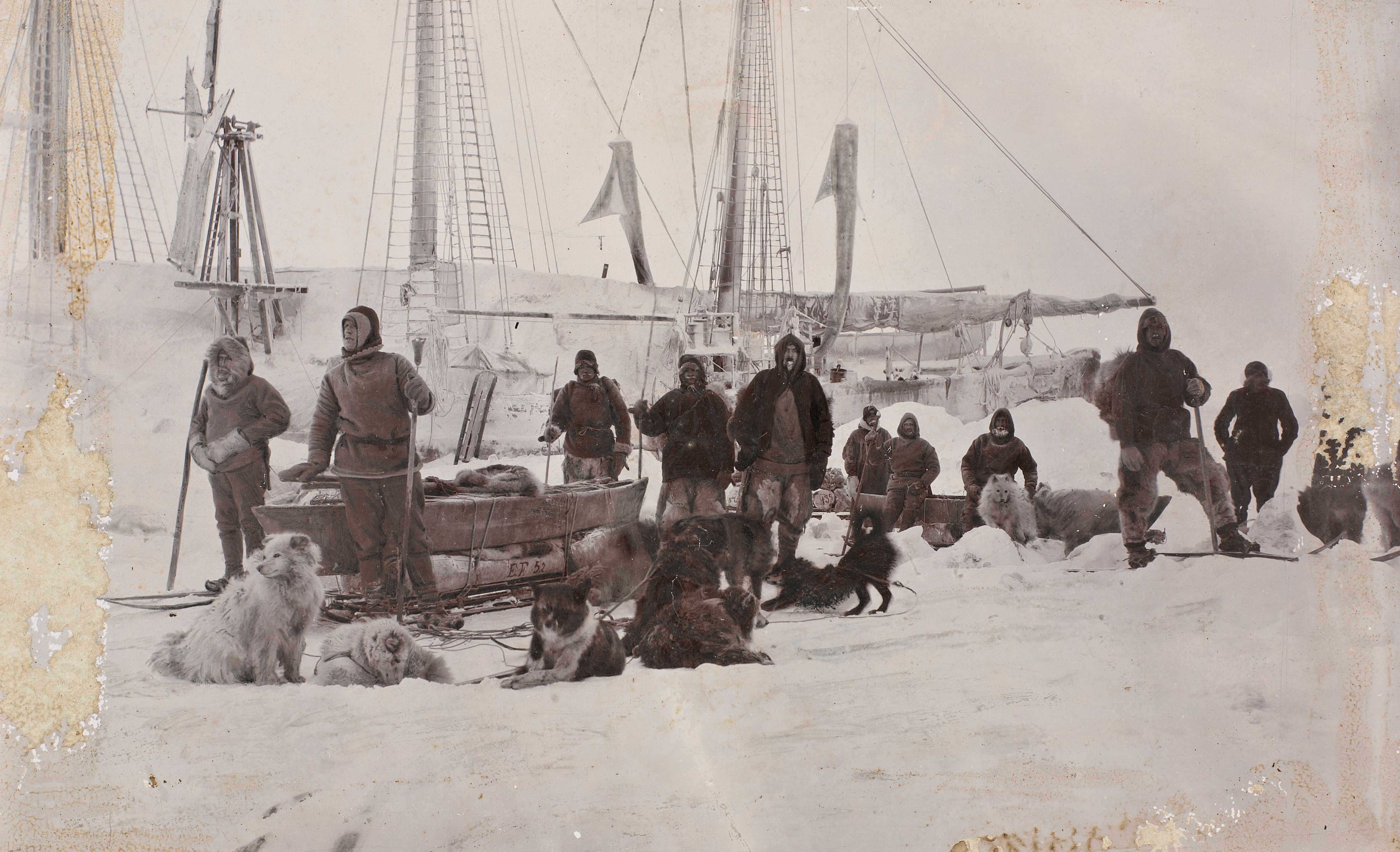 Fridtjof Nansen's crew with their luggage and dogs standing in the snow in front of a boat