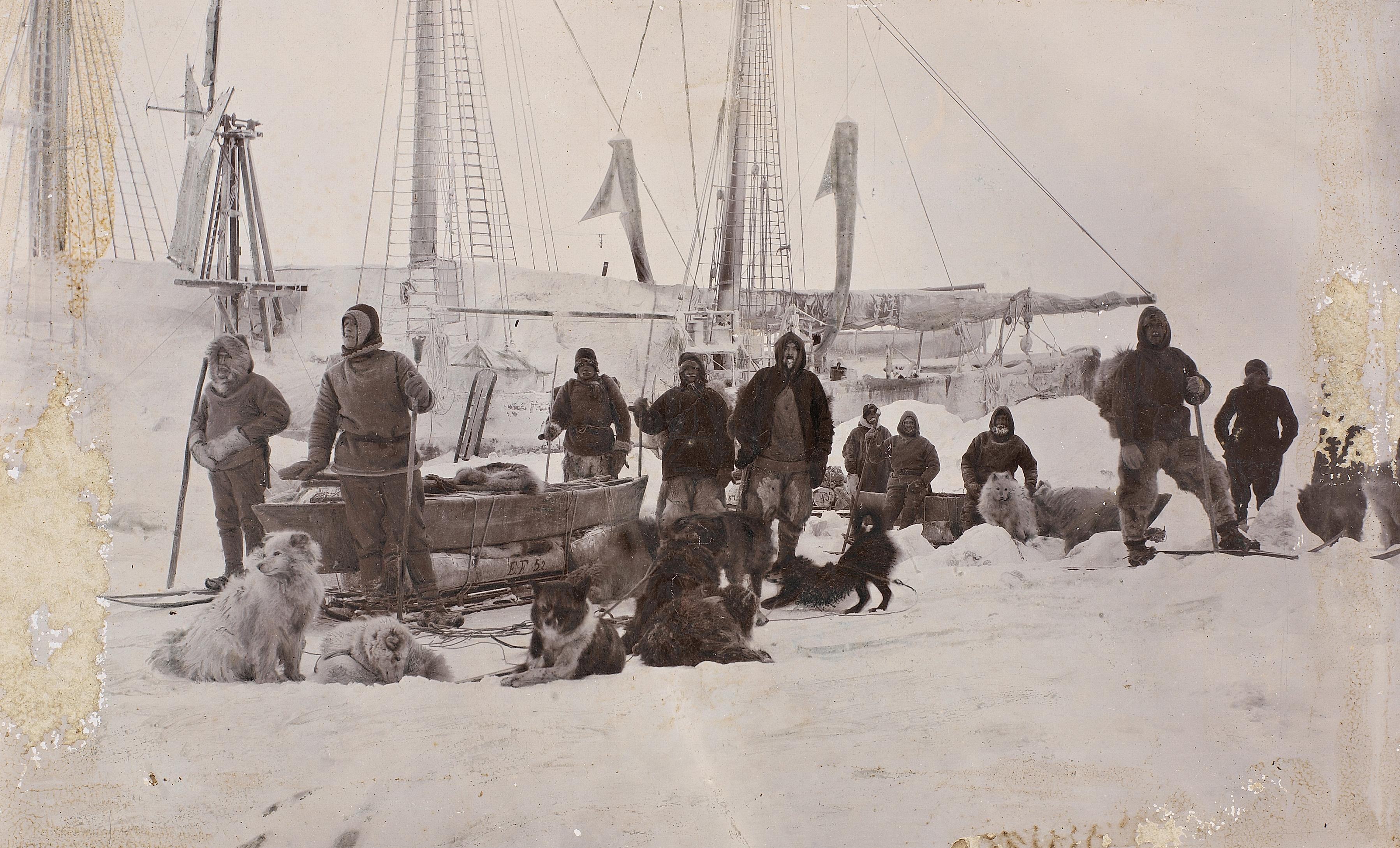 Fridtjof Nansen's crew with their luggage and dogs standing in the snow in front of a boat