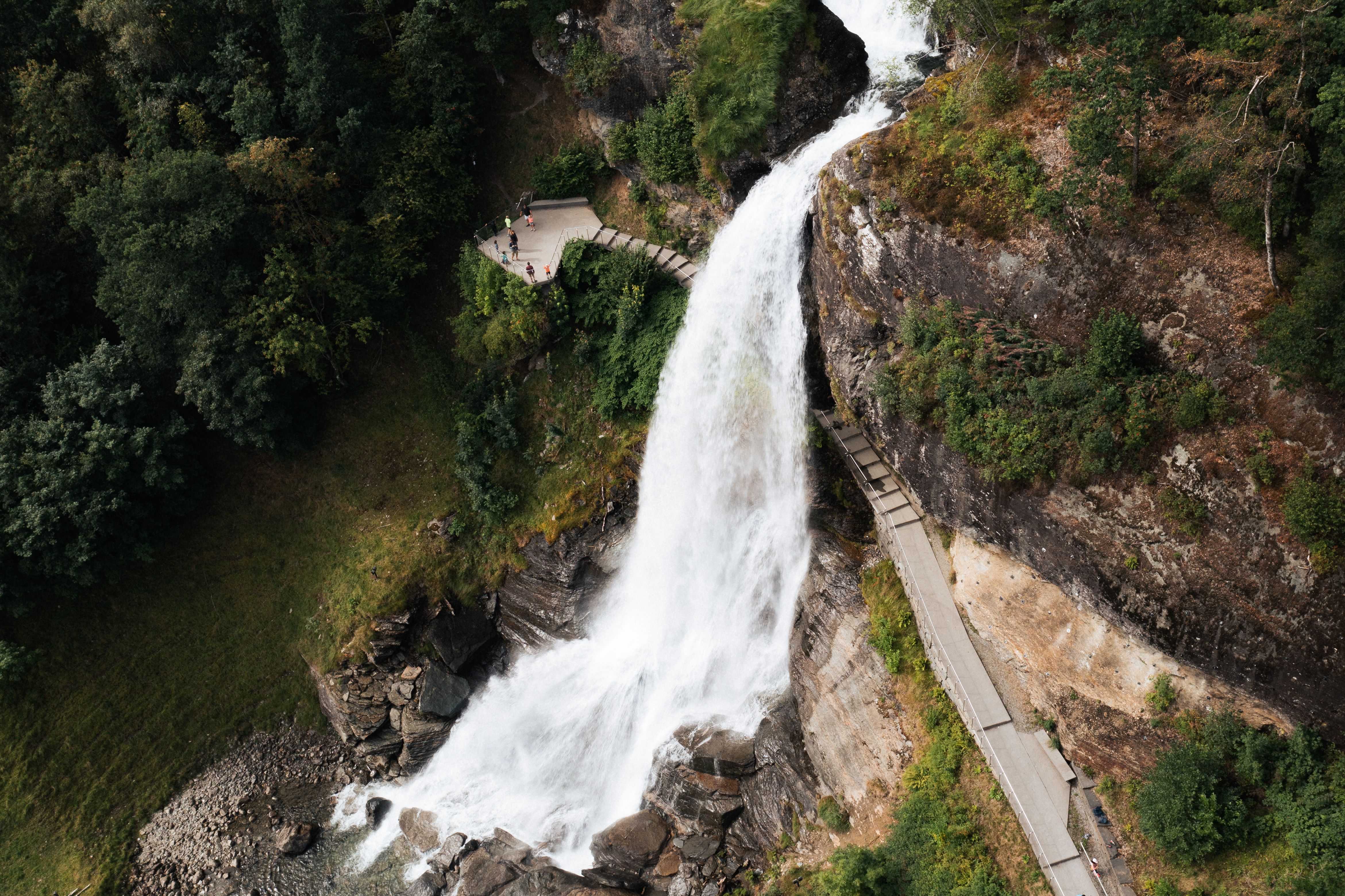 A water fall rushing down a mountain with people walking behind it.