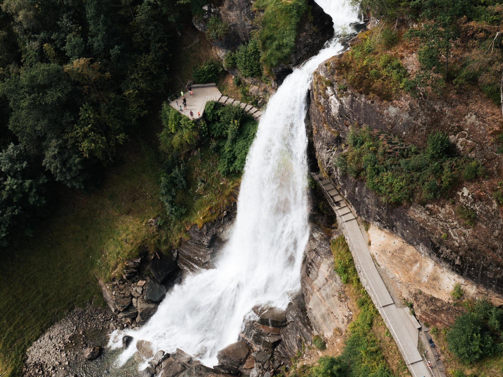 A water fall rushing down a mountain with people walking behind it.