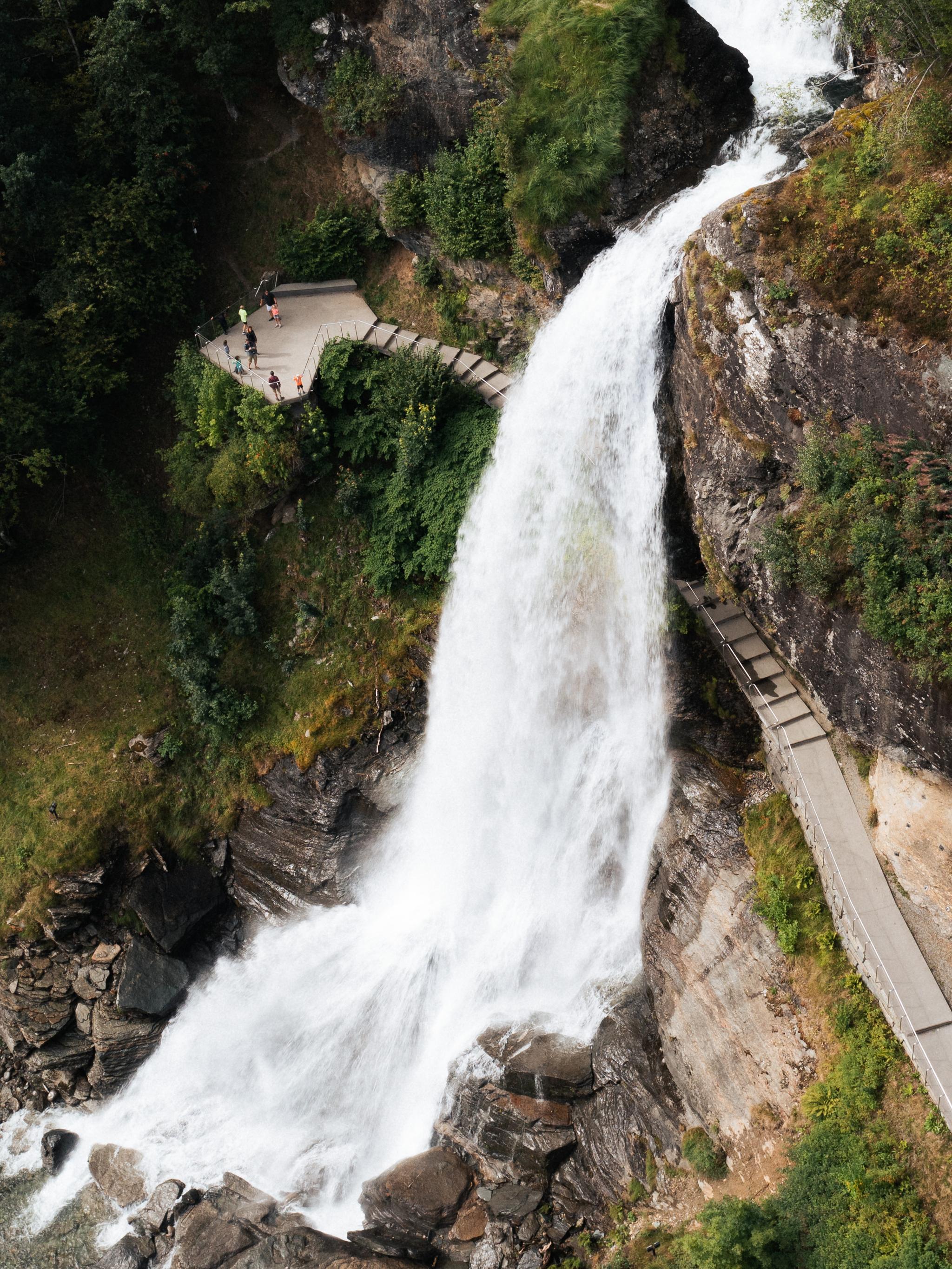A water fall rushing down a mountain with people walking behind it.