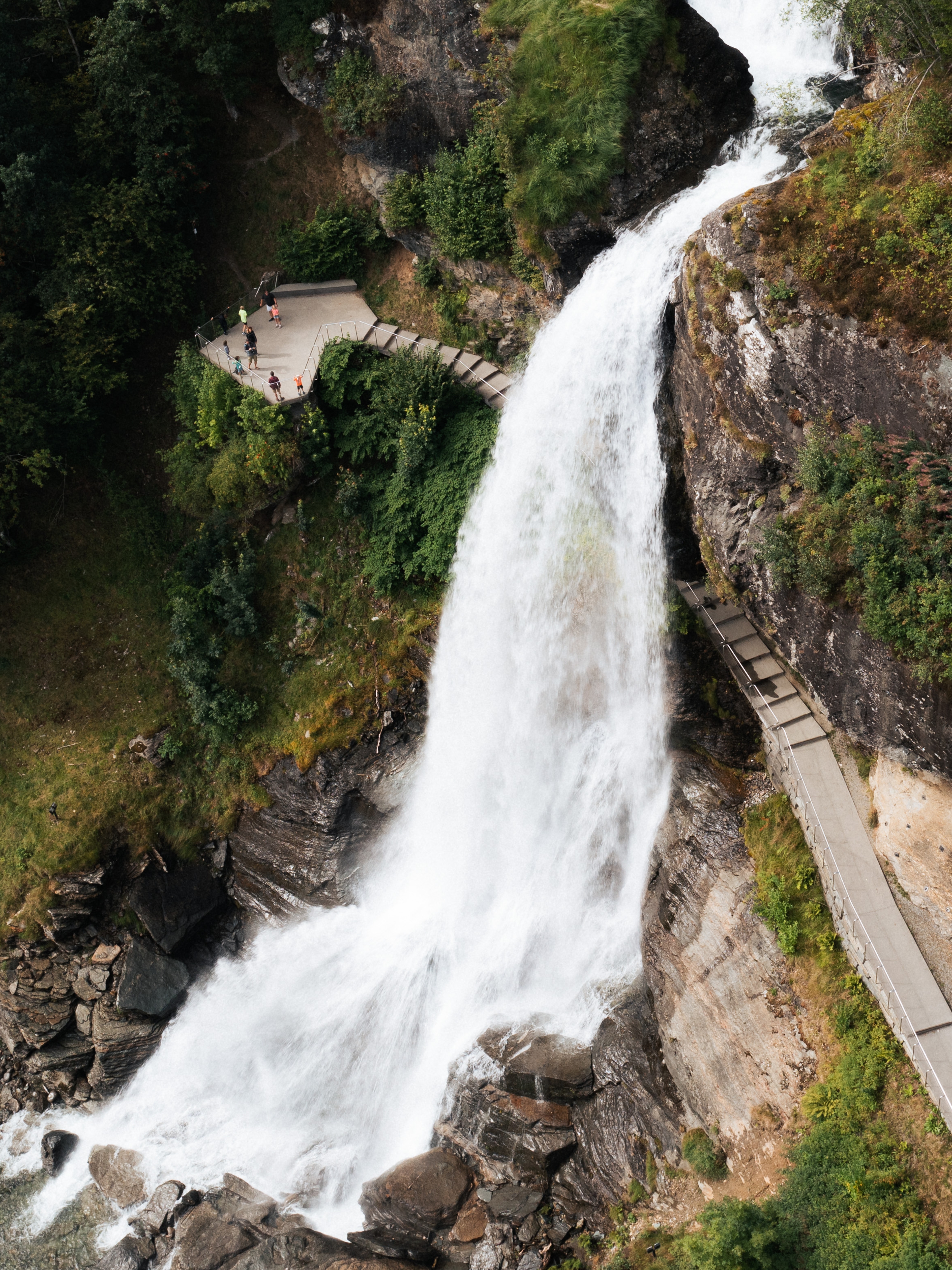 A water fall rushing down a mountain with people walking behind it.