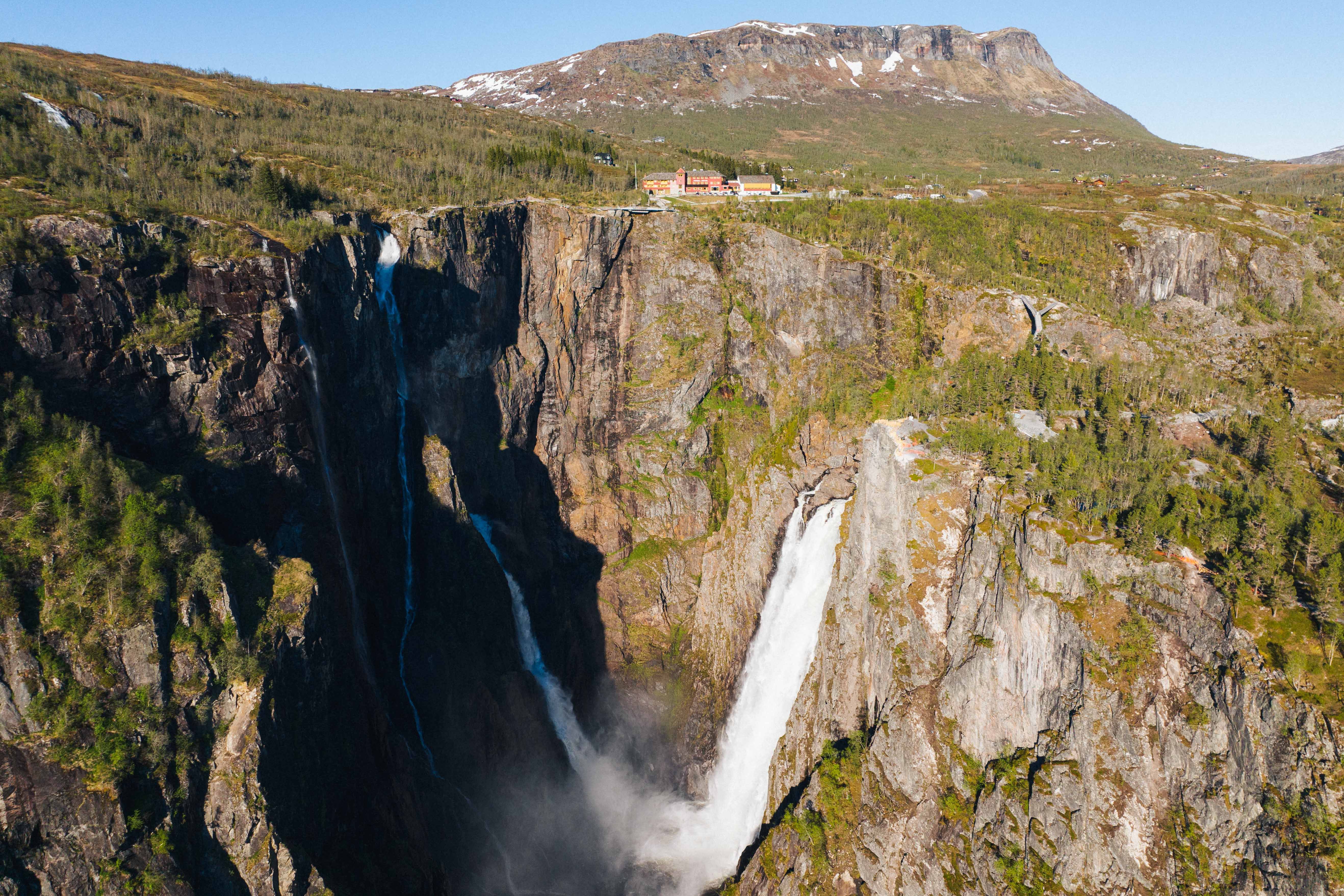 A huge waterfall and a building on a mountain ledge