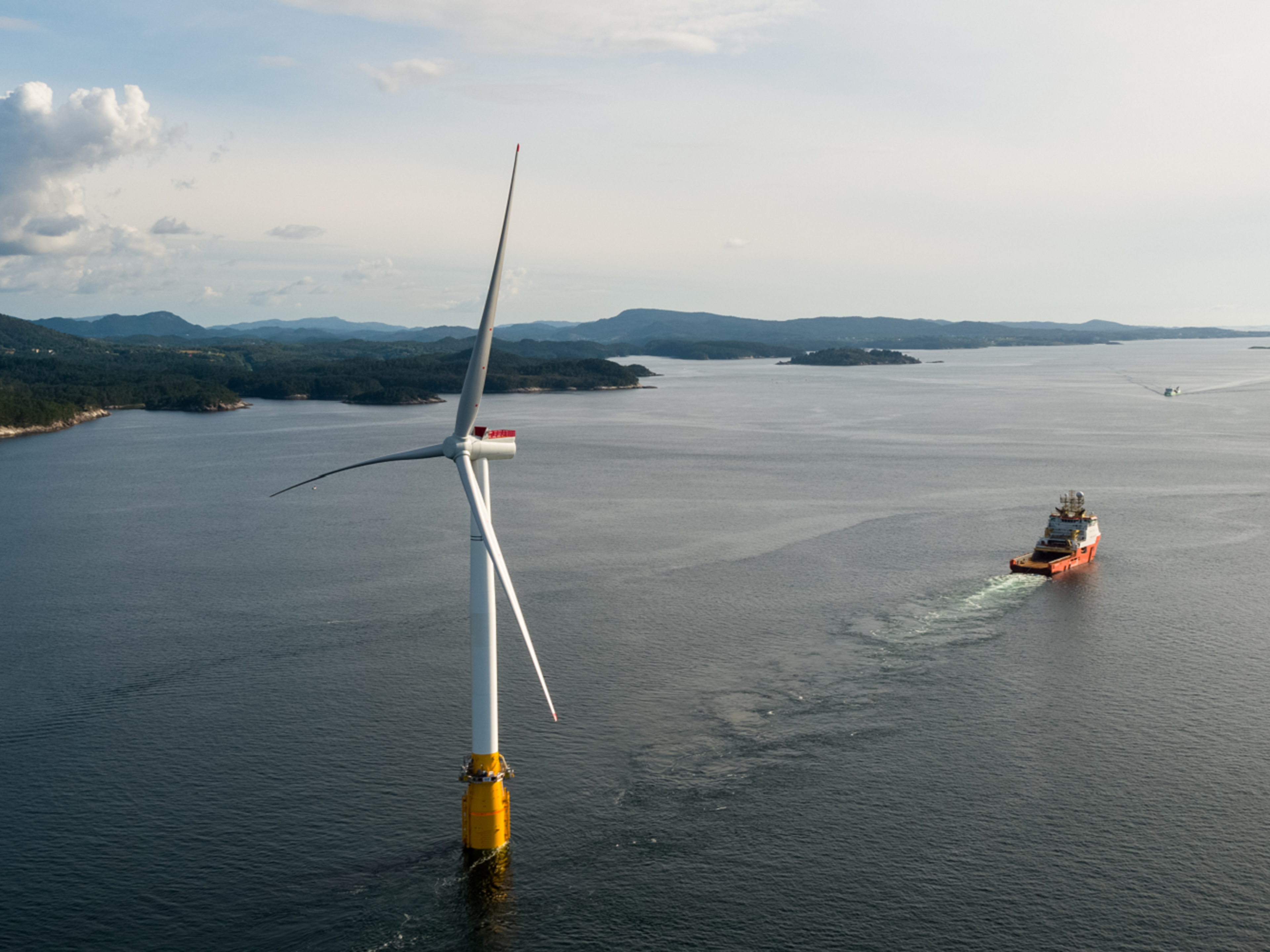 Floating offshore wind turbine in coastal setting with offshore vessel in the distance