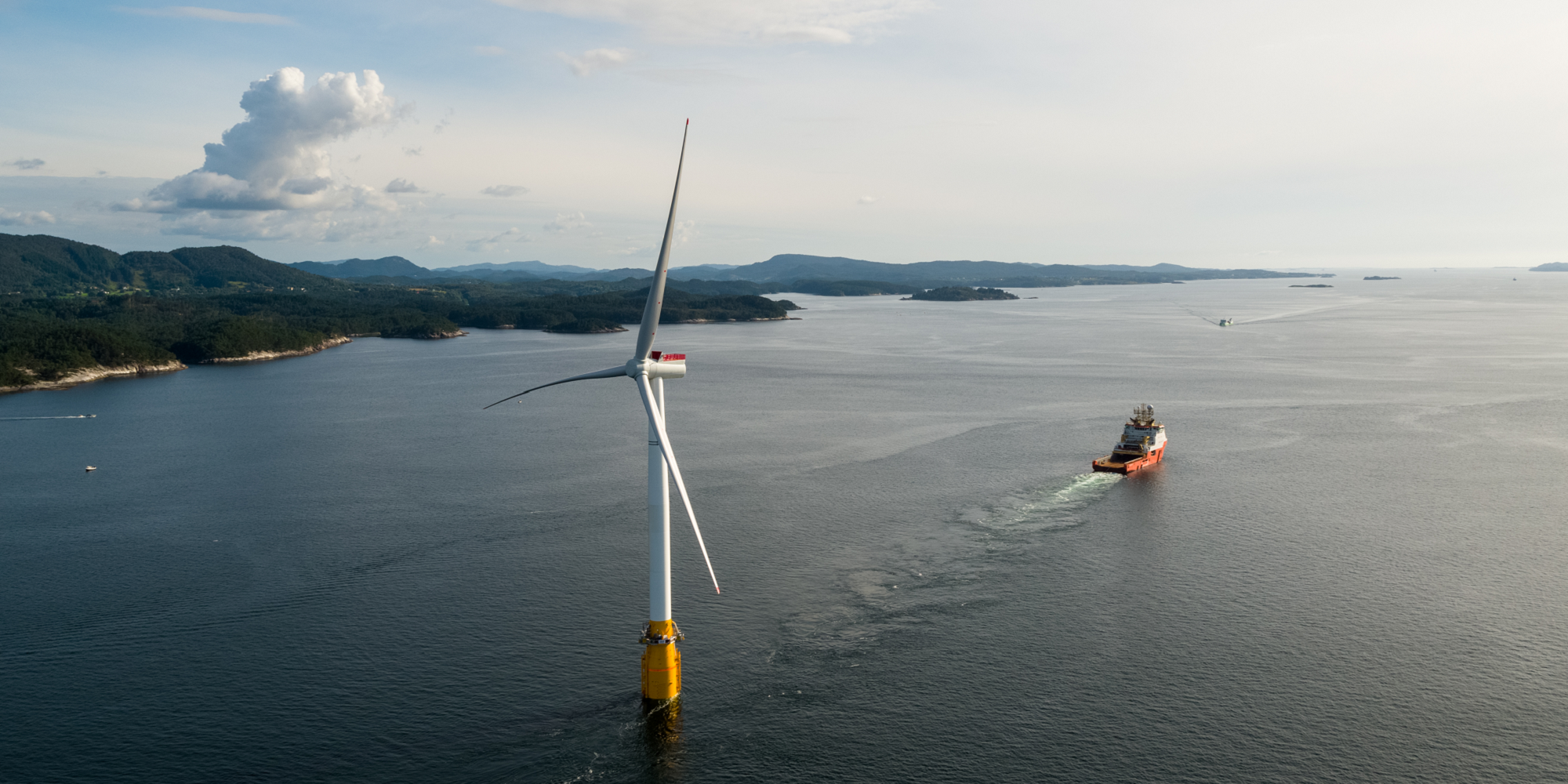 Floating offshore wind turbine in coastal setting with offshore vessel in the distance