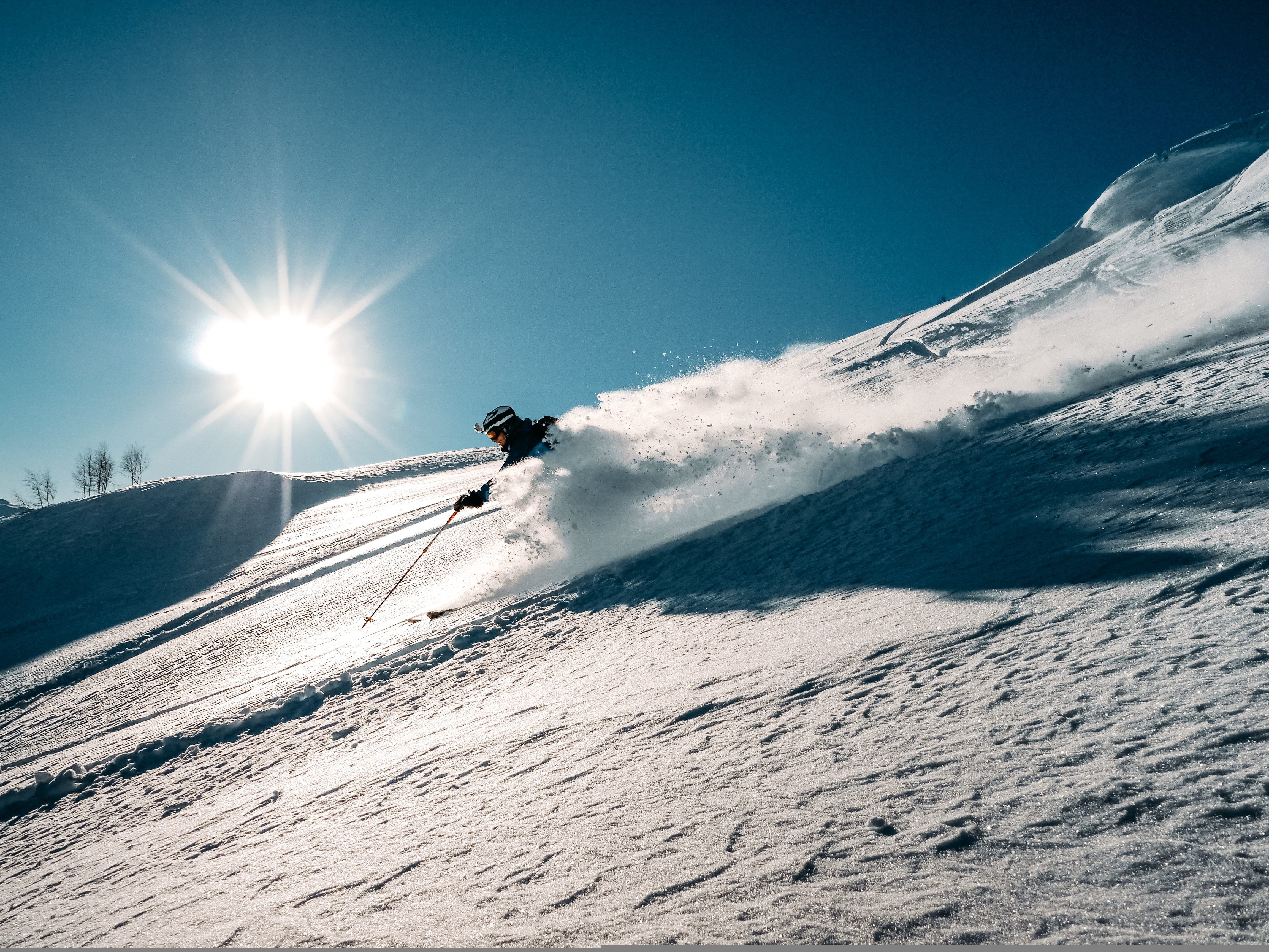 A skiier coming down a slope with a rush of powdery snow.