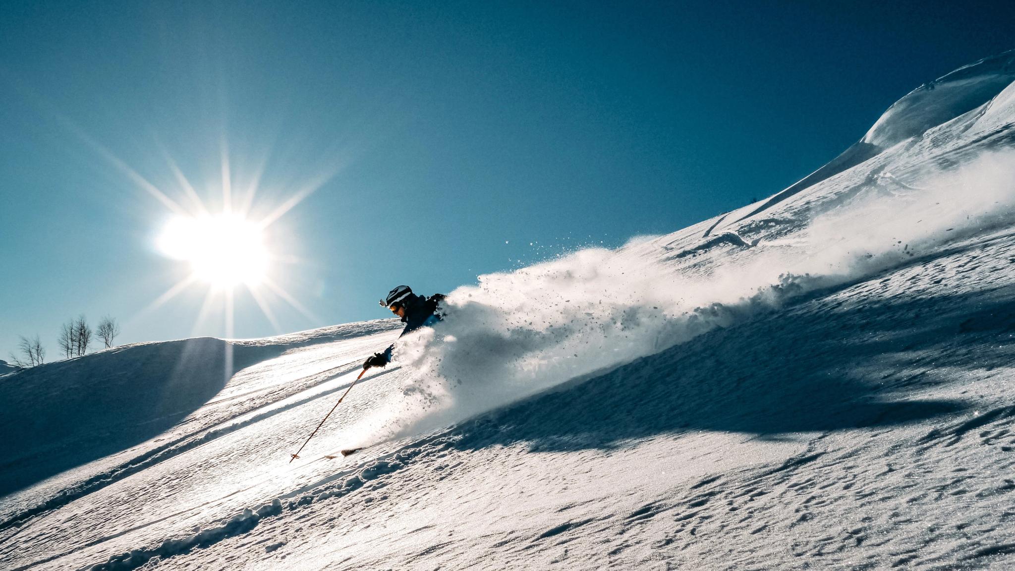 A skiier coming down a slope with a rush of powdery snow.