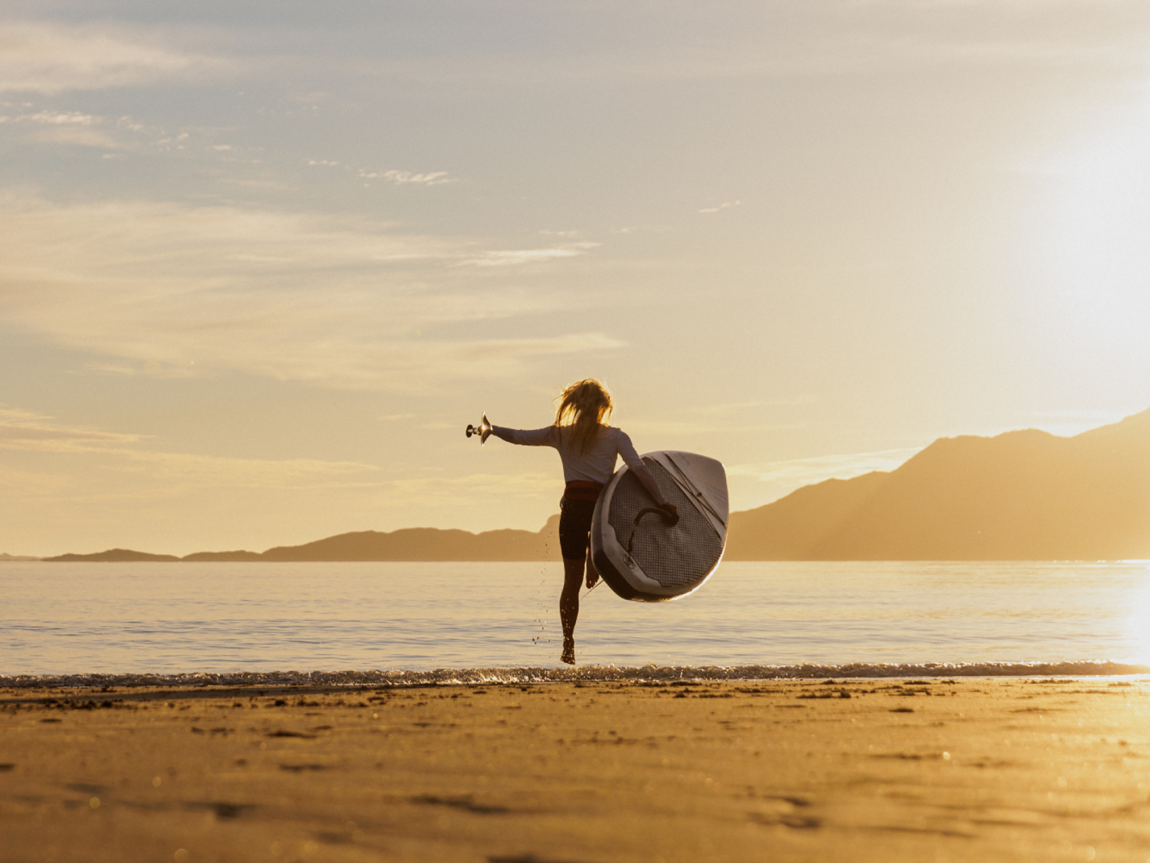 A woman going out in the water with a paddle board in the midnight sun, Northern Norway.