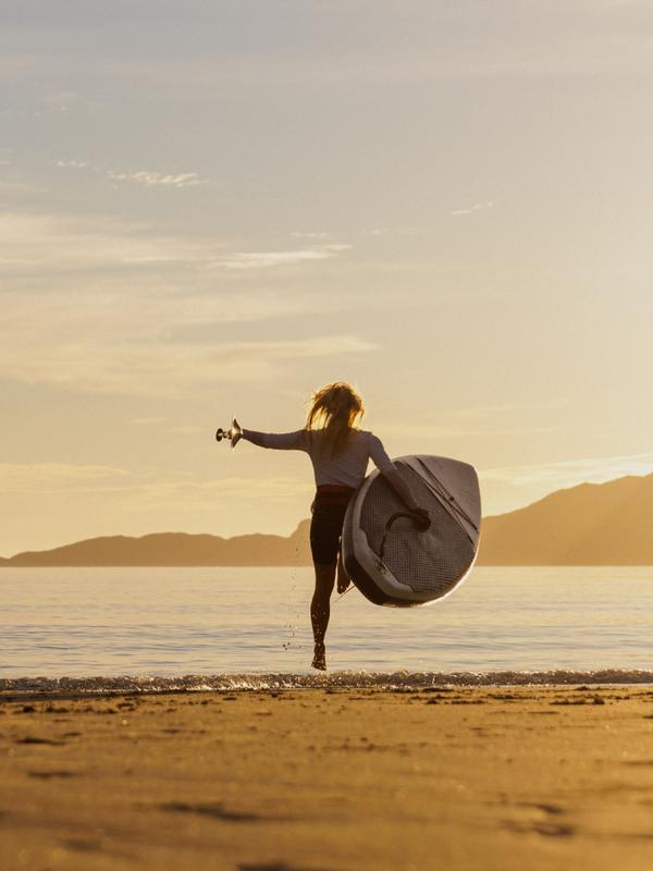 A woman going out in the water with a paddle board in the midnight sun, Northern Norway.