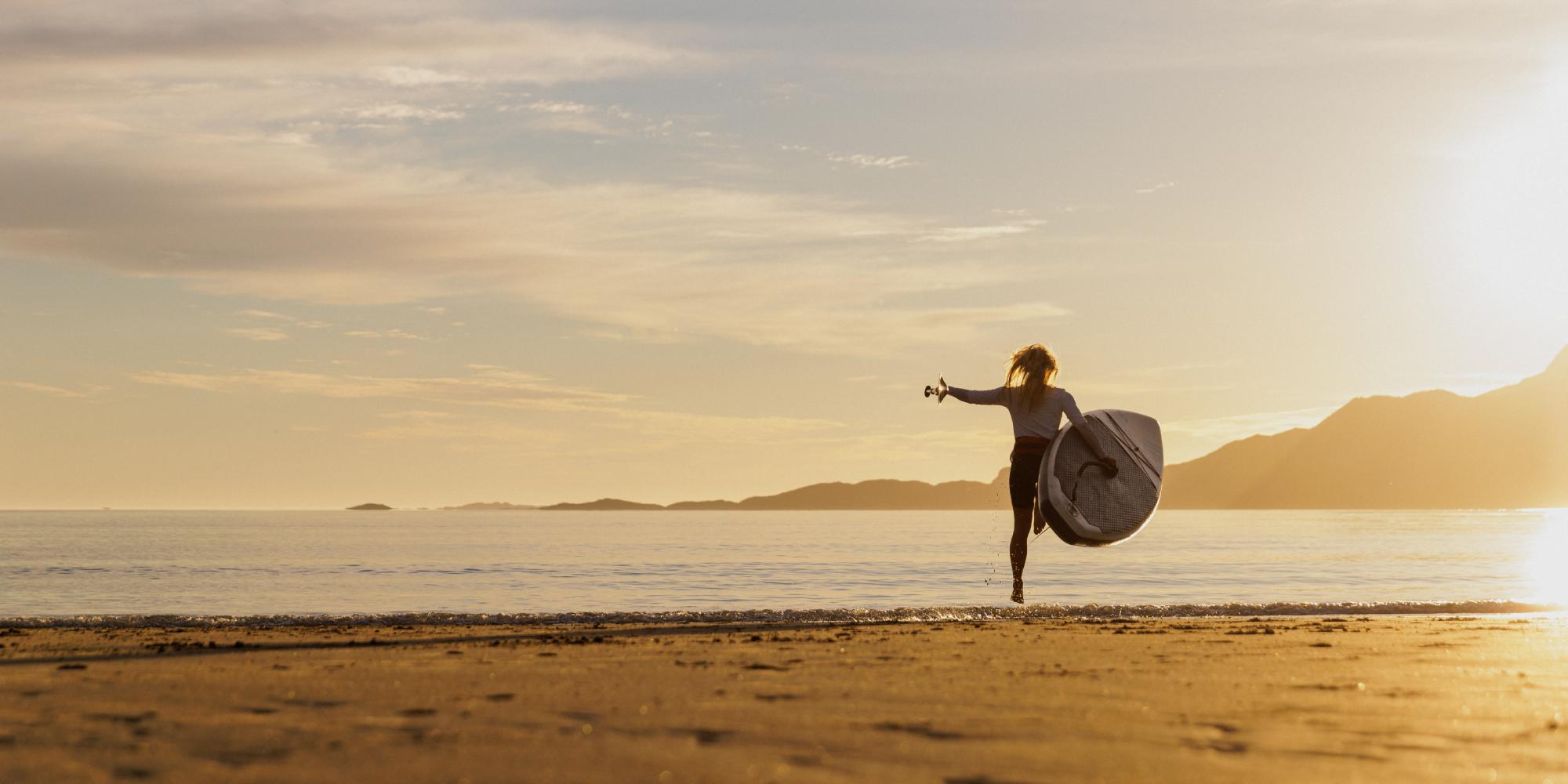 A woman going out in the water with a paddle board in the midnight sun, Northern Norway.