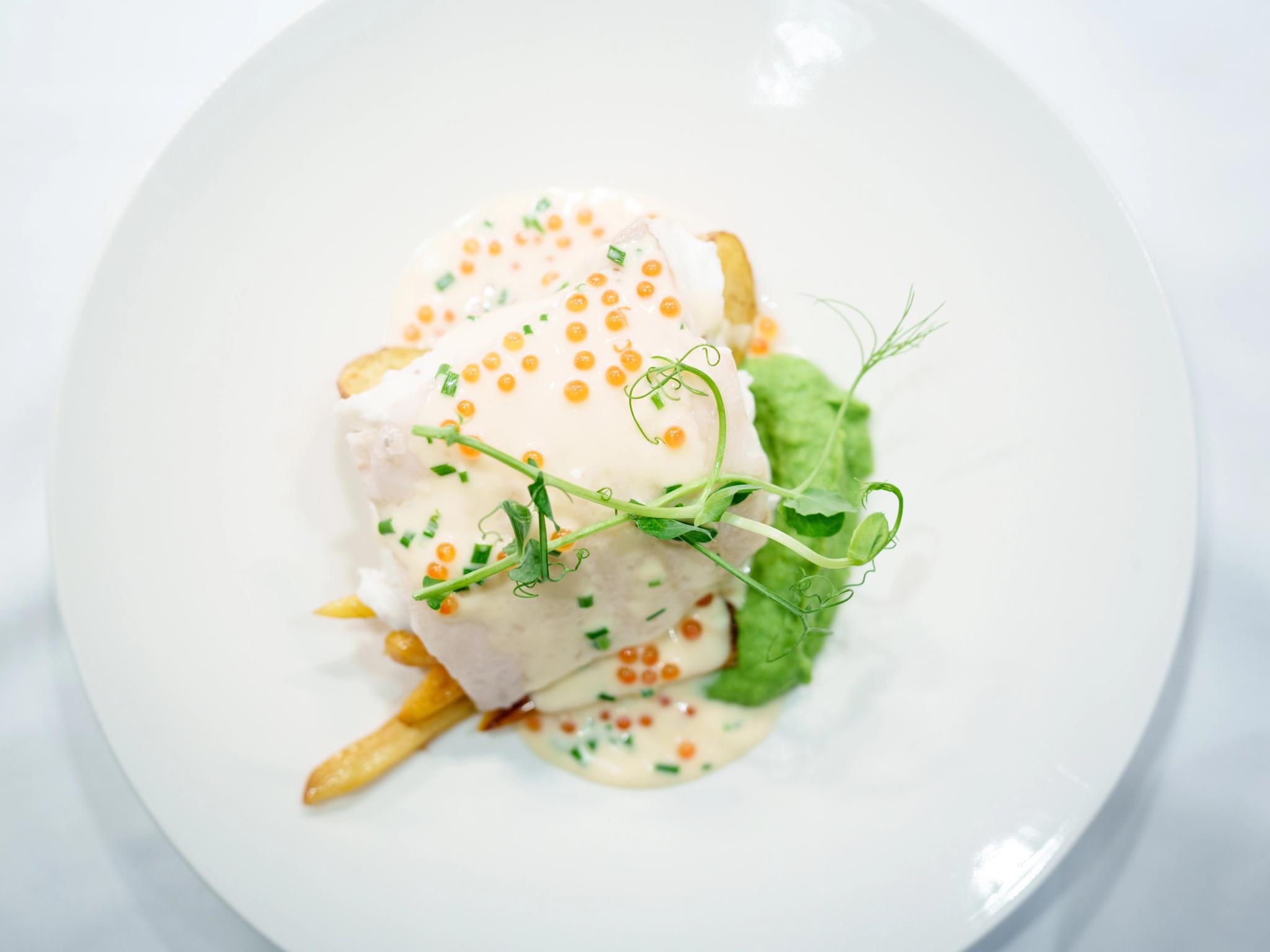 A plated dish of halibut, potatoes, pea puree and a white sauce.