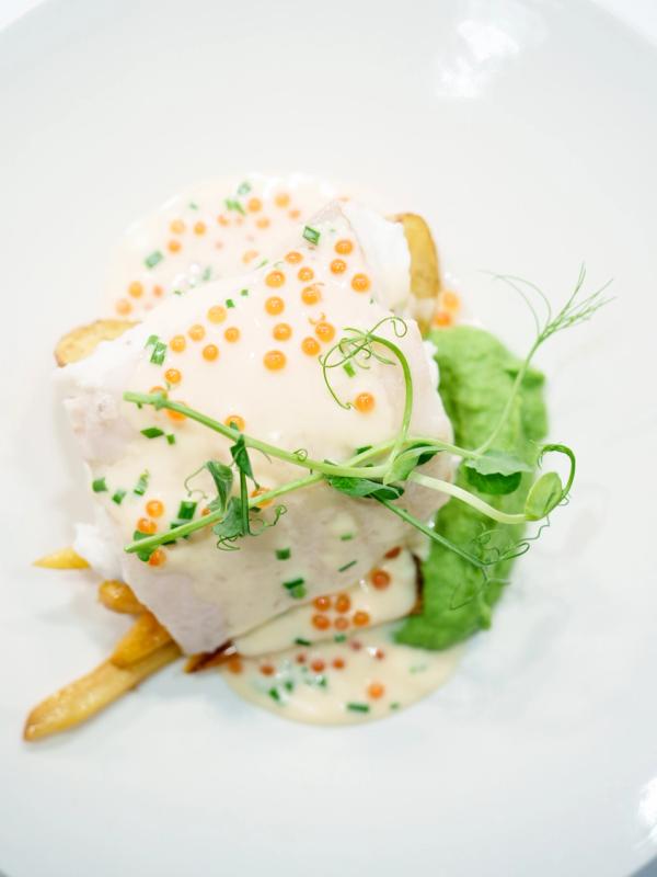 A plated dish of halibut, potatoes, pea puree and a white sauce.