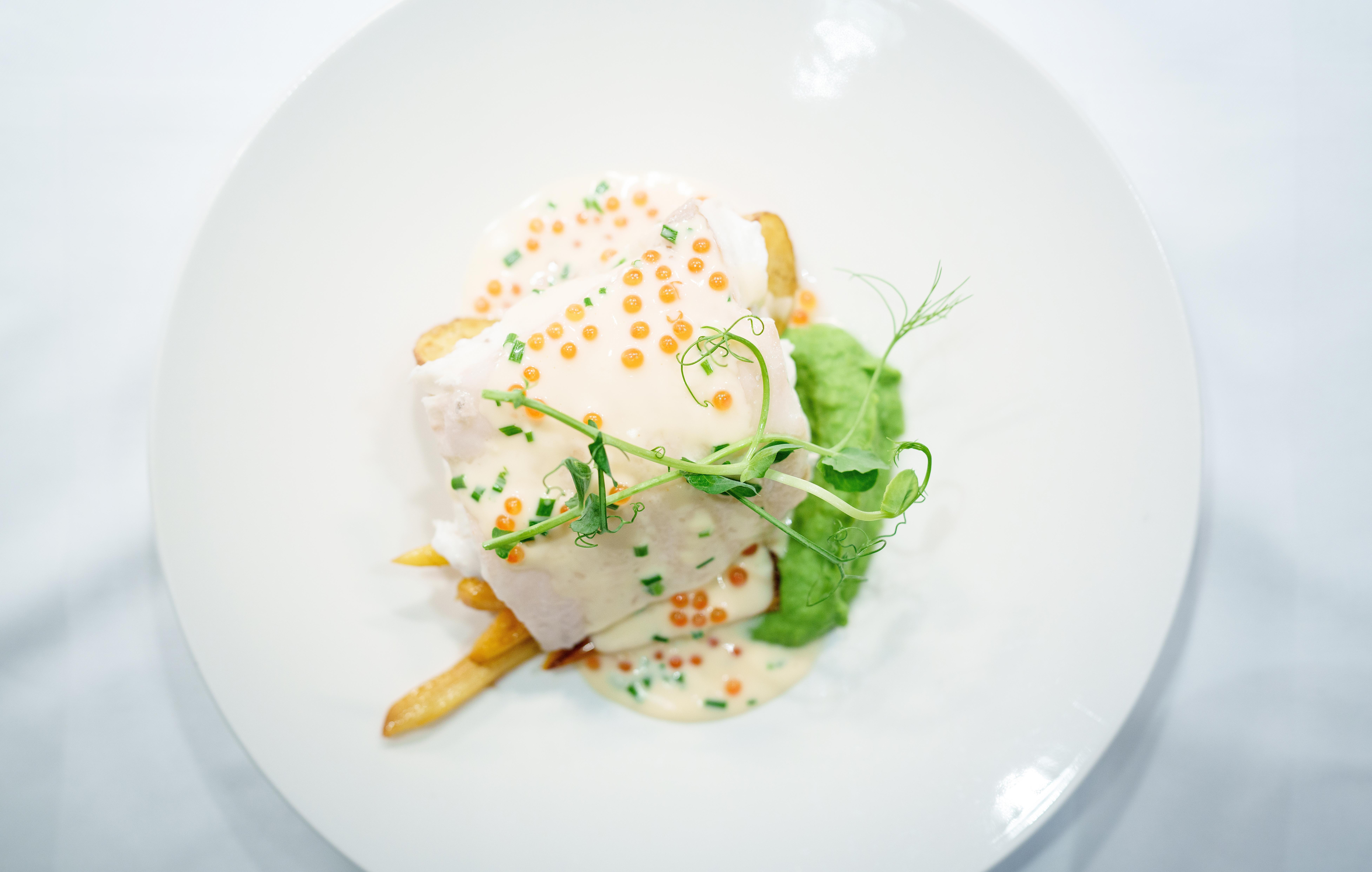 A plated dish of halibut, potatoes, pea puree and a white sauce.