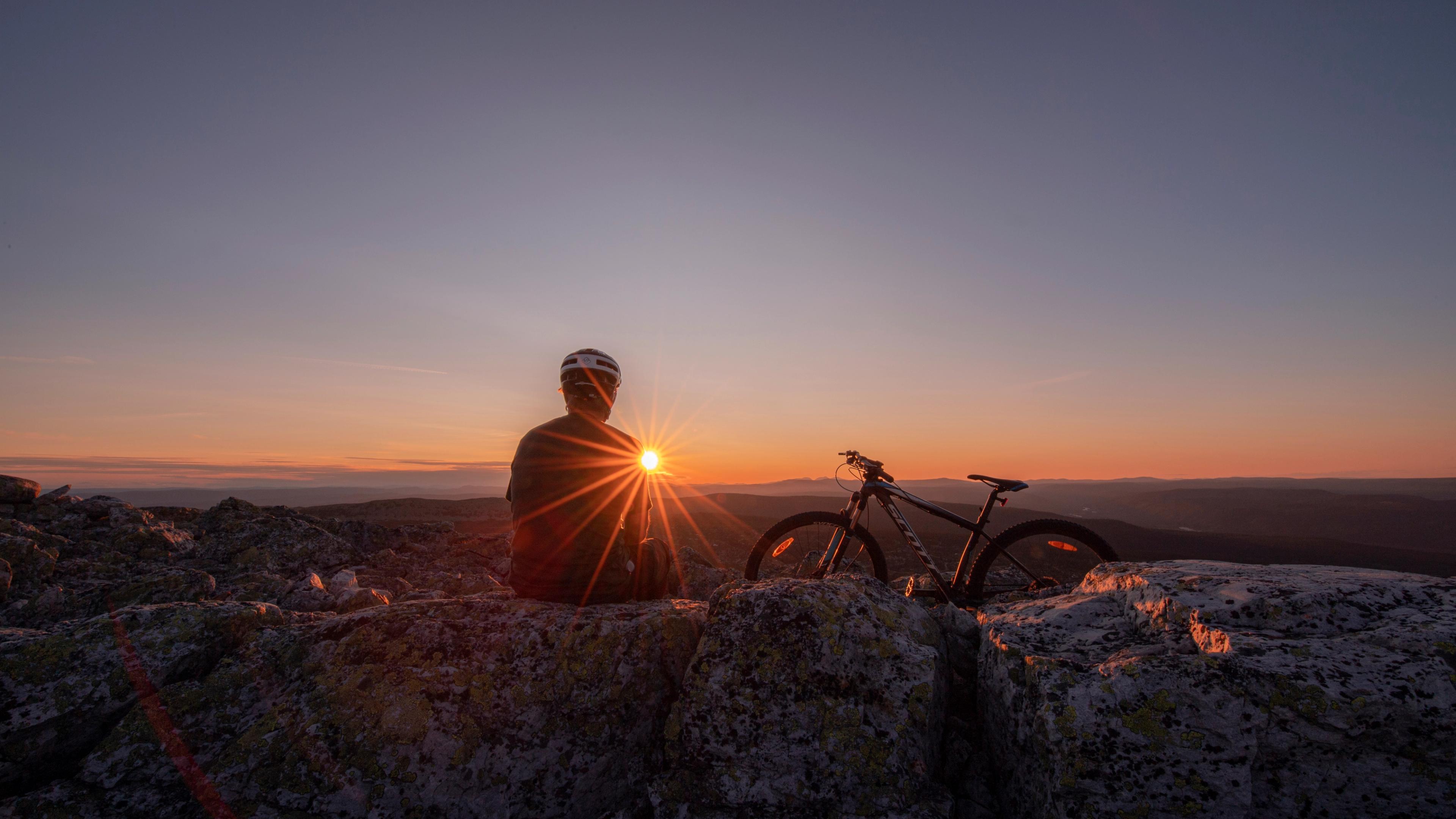 A person is enjoying a break while biking in the mountains of Trysil, watching the sun set.