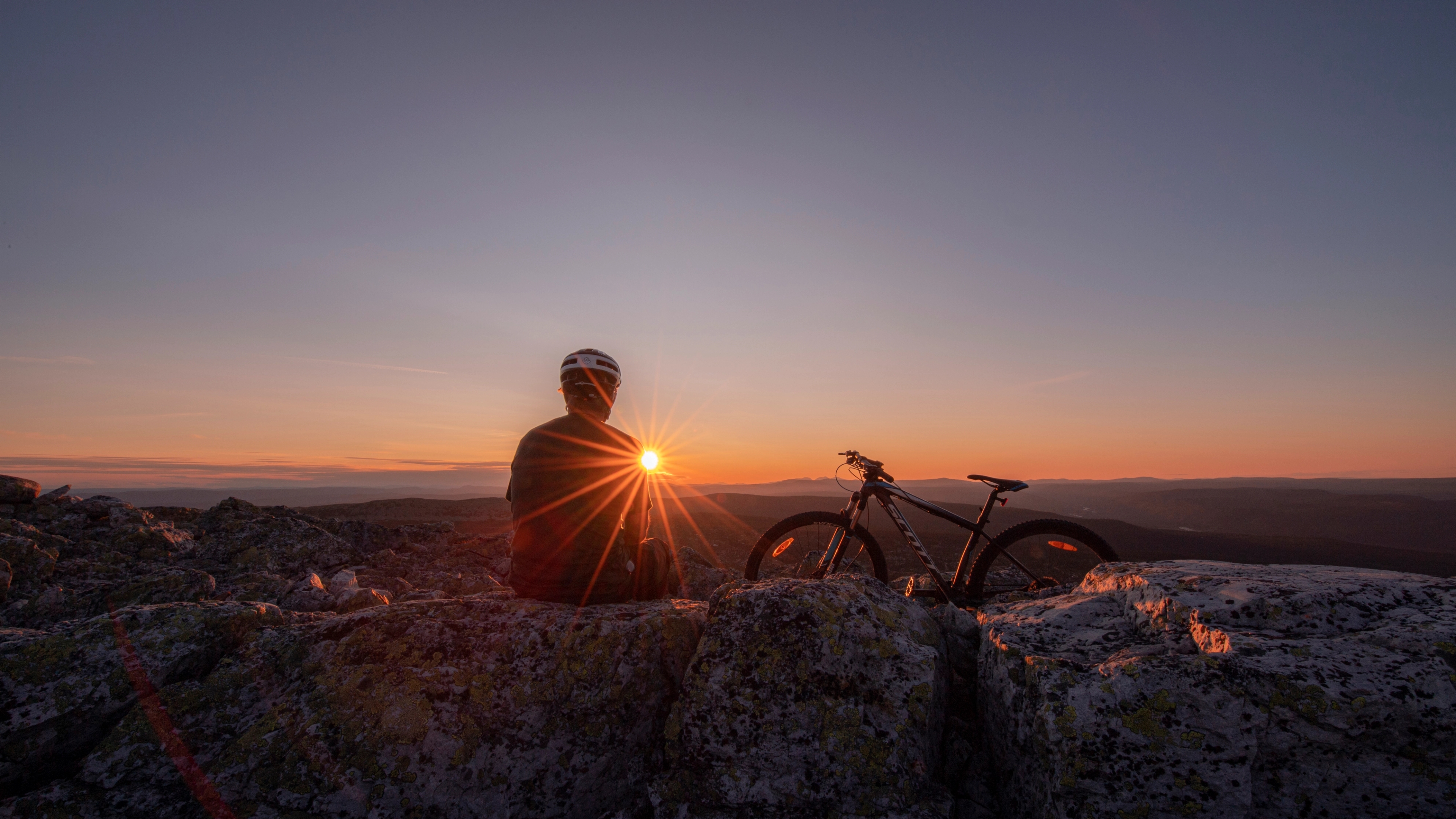 A person is enjoying a break while biking in the mountains of Trysil, watching the sun set.