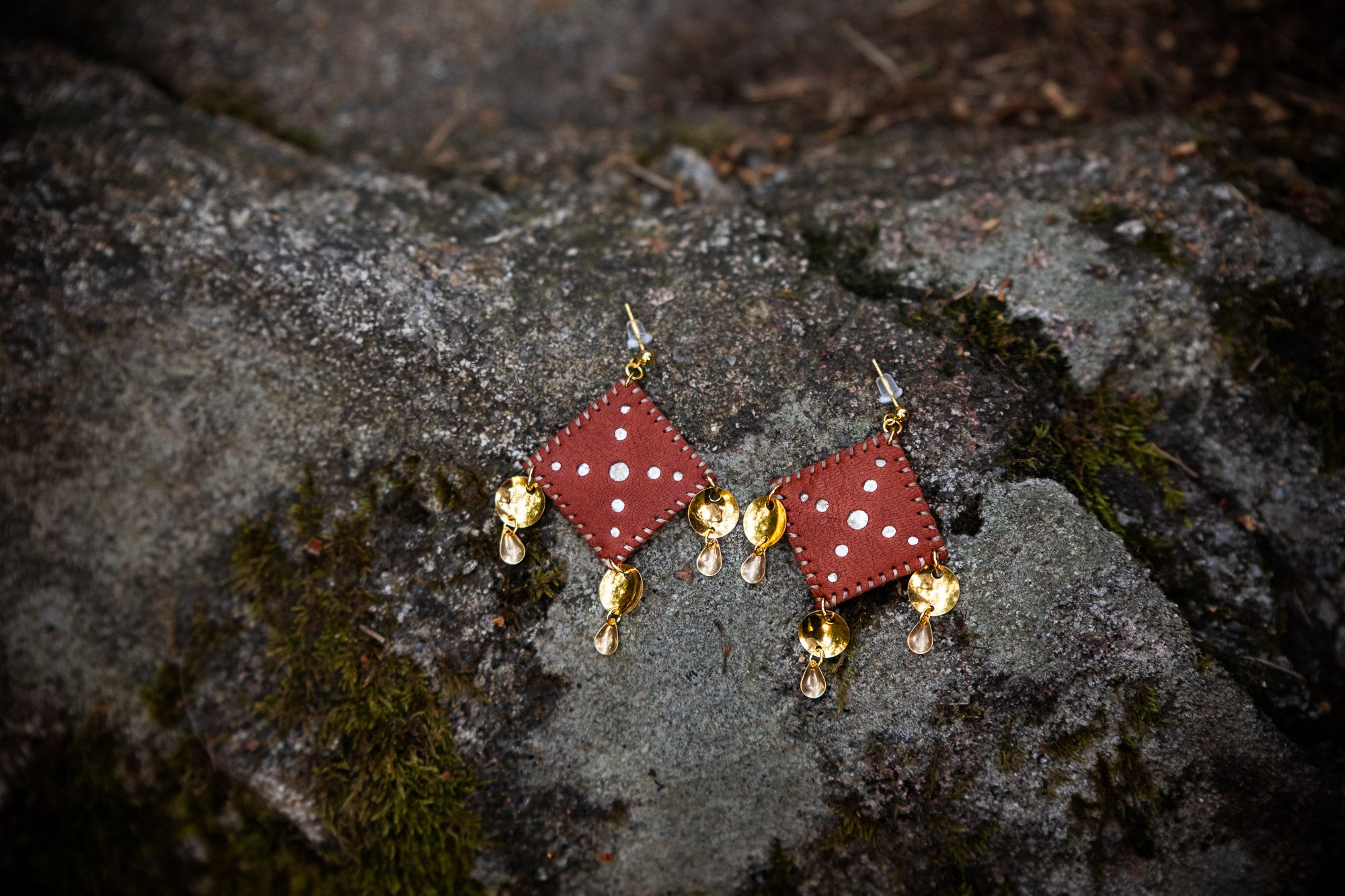 Leather and gold Sami inspired earrings resting on a rock