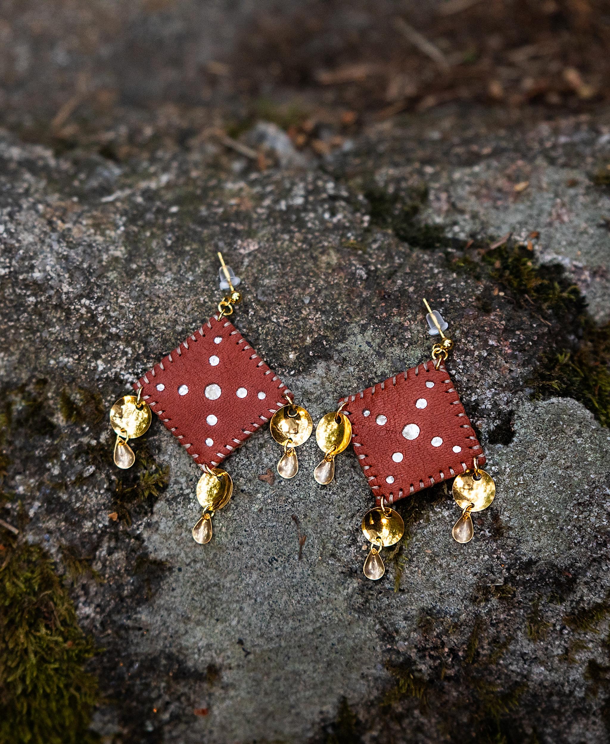 Leather and gold Sami inspired earrings resting on a rock