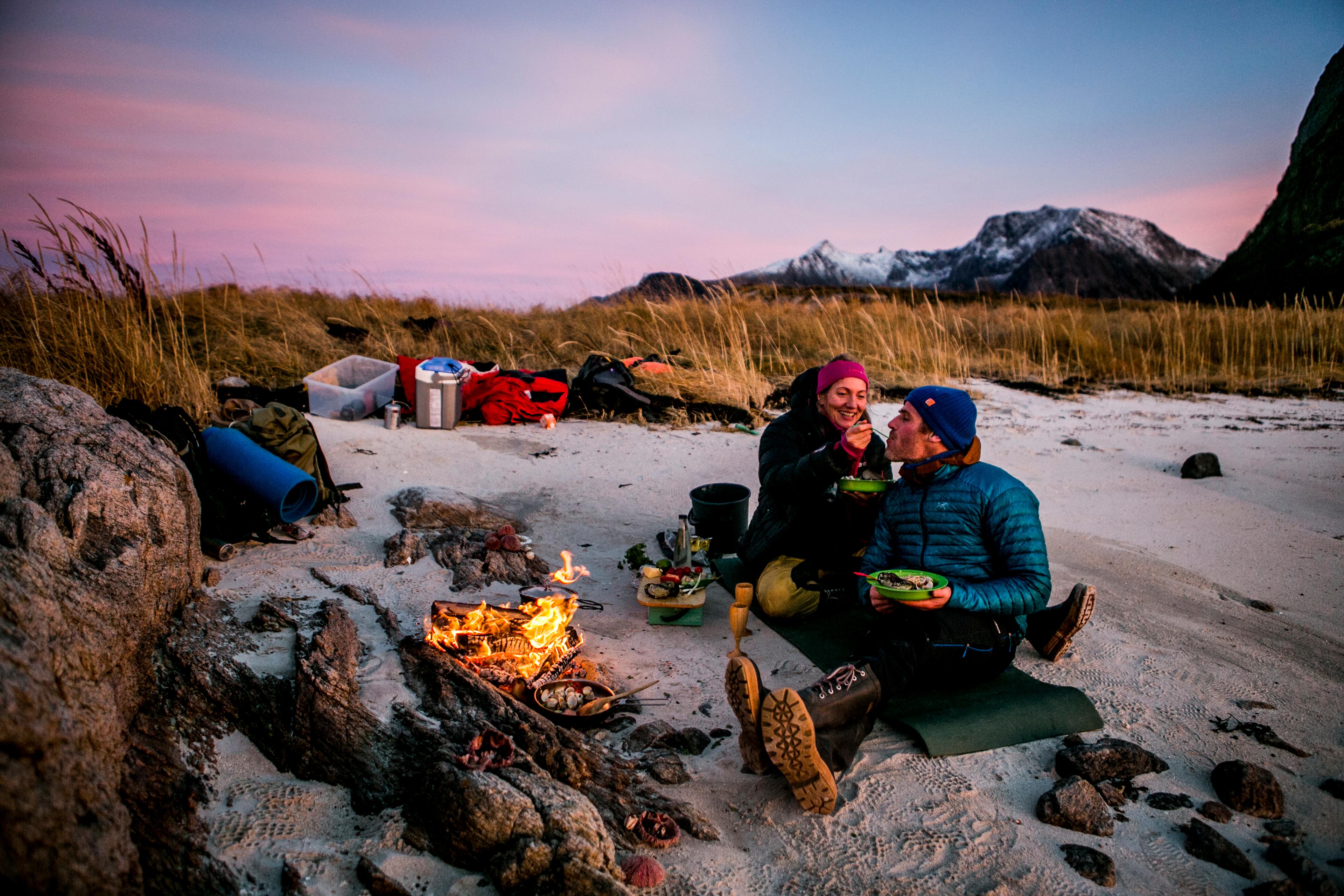 Et par spiser middag ved bålet på stranden i Steigen i Nordland, Nord-Norge
