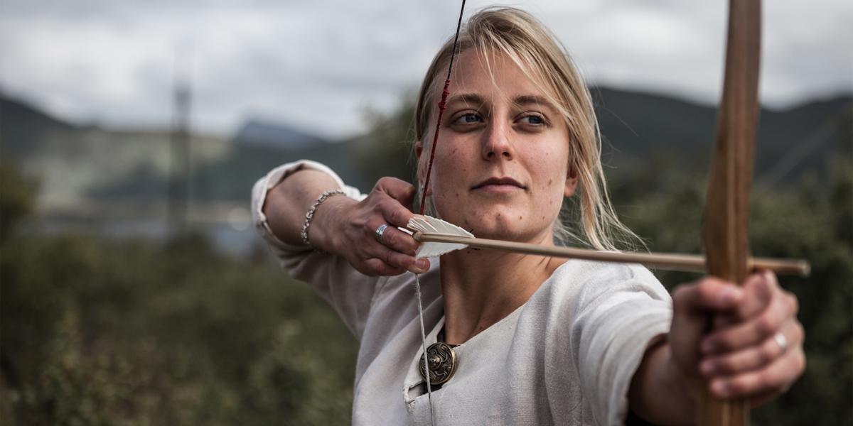 En dame skyter med pil og bue på Lofotr Vikingmuseum på Borg, en av Norges største vikingopplevelser