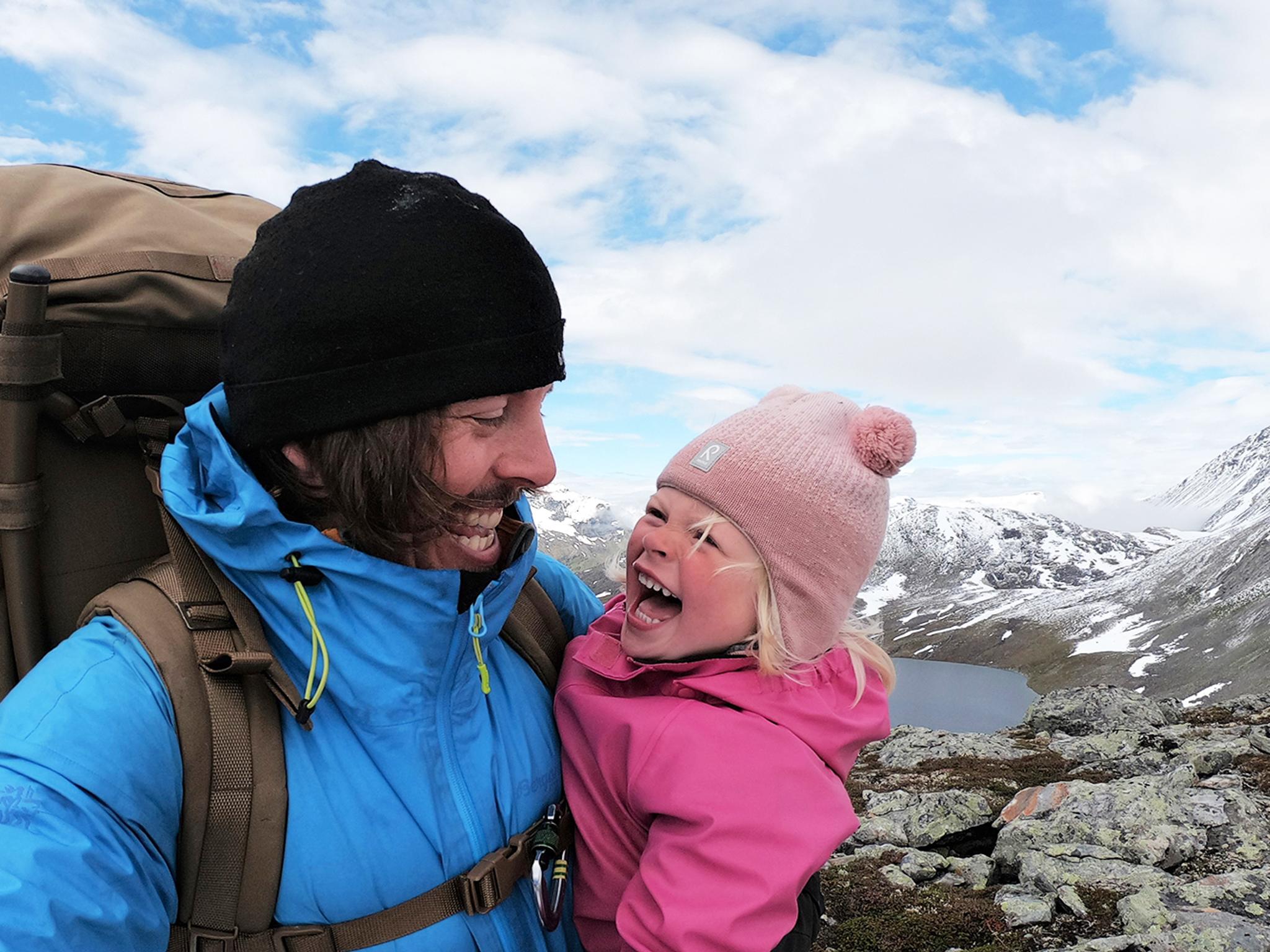 Nærbilde av en ung jente og pappaen hennes som smiler til hverandre på vandretur i Hjørundfjorden på Vestlandet