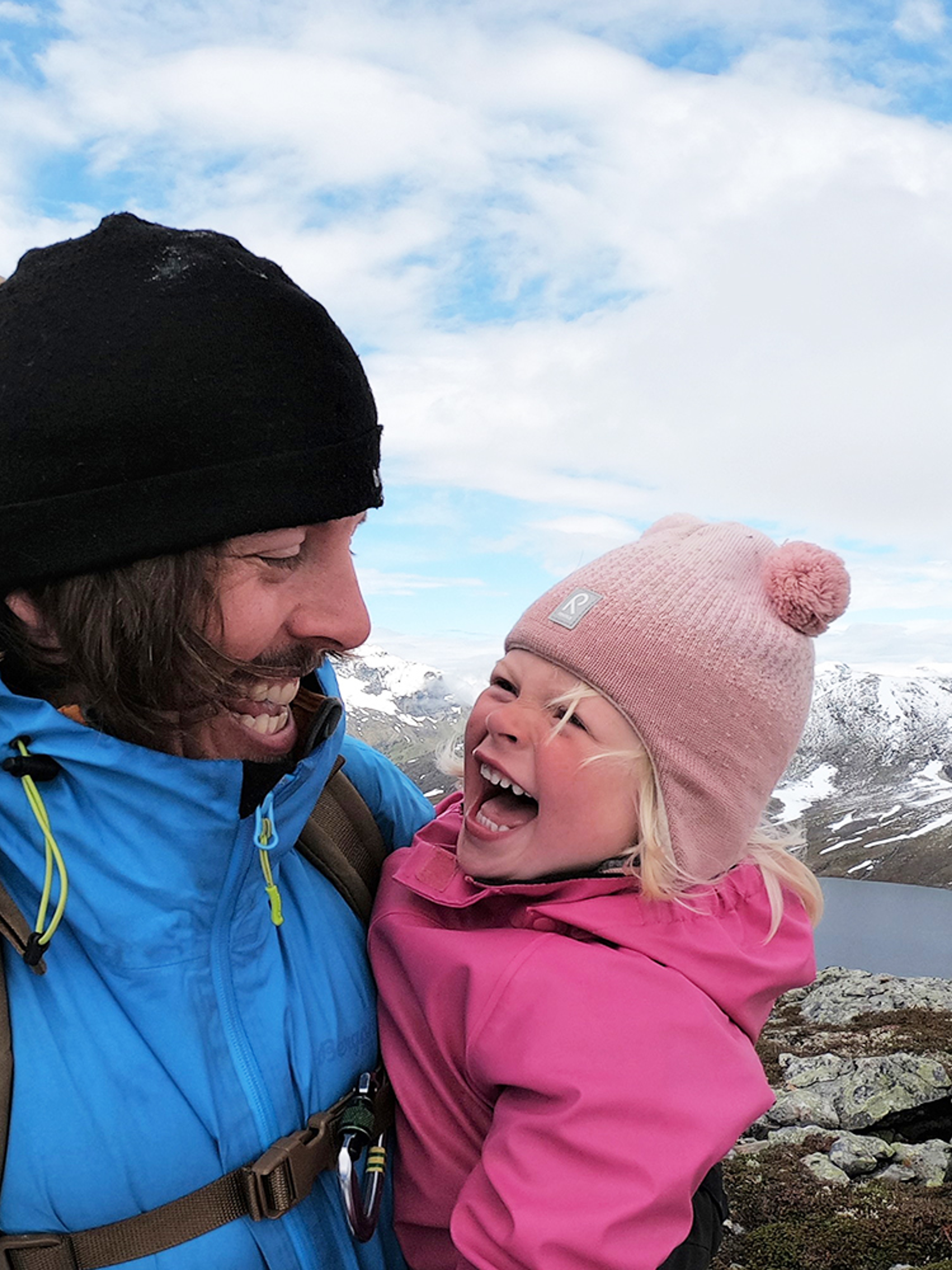 Close-up image of a young girl and her father smiling at each other on a hiking trip in Hjørundfjorden, Fjord Norway