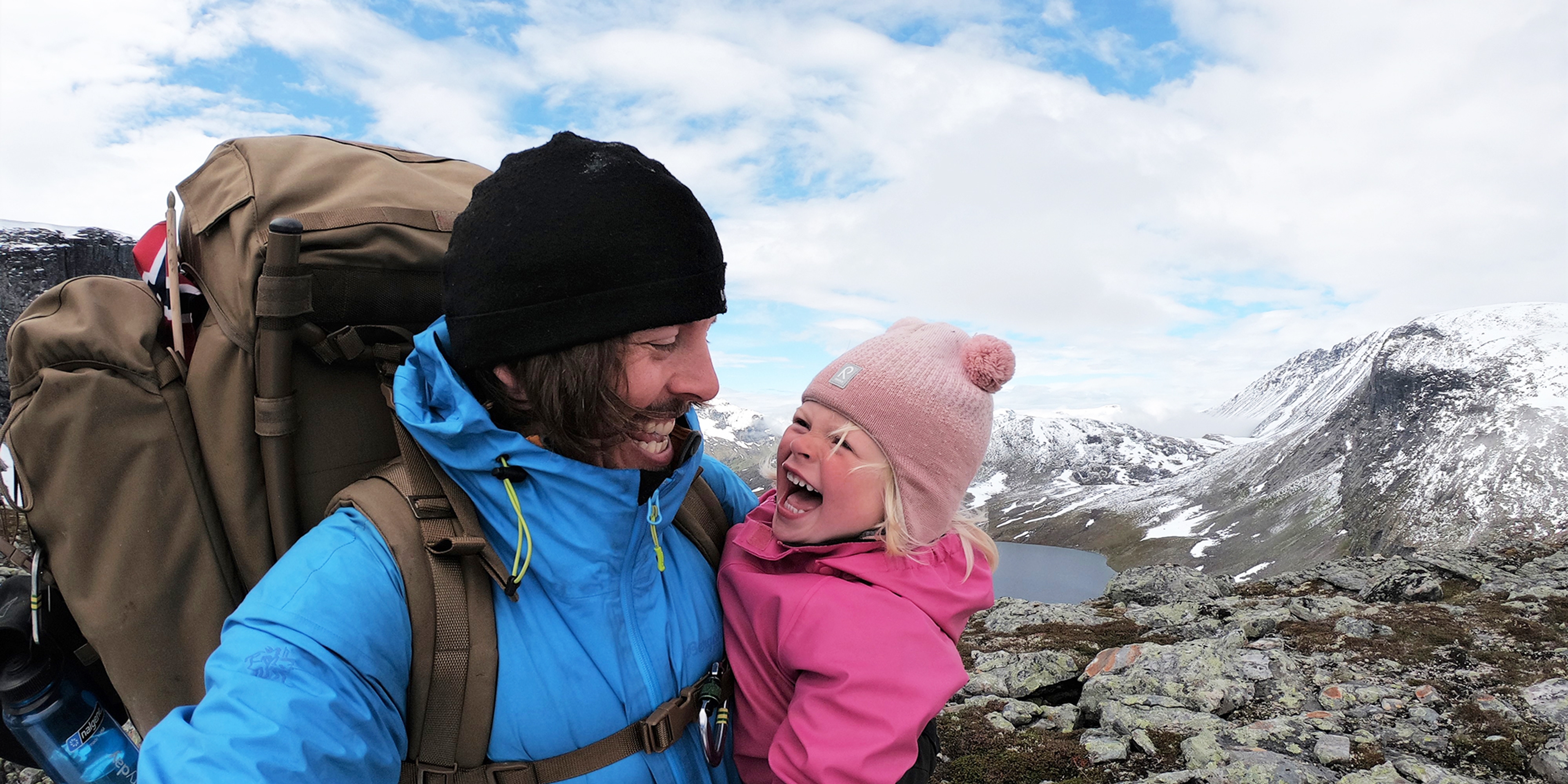 Close-up image of a young girl and her father smiling at each other on a hiking trip in Hjørundfjorden, Fjord Norway
